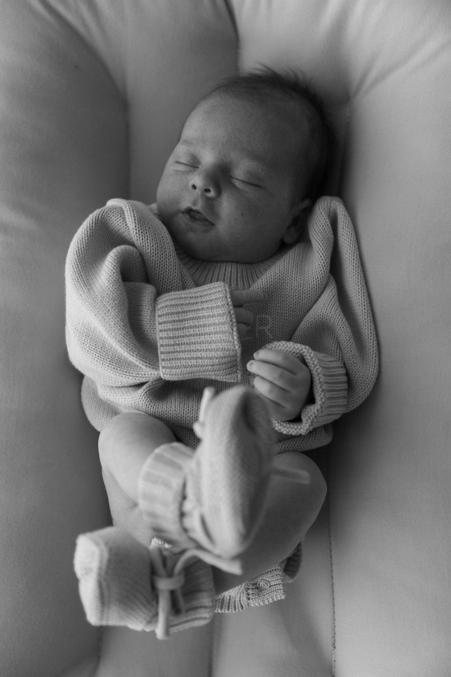 Peaceful black and white portrait of a sleeping newborn baby wrapped in a soft knit blanket.