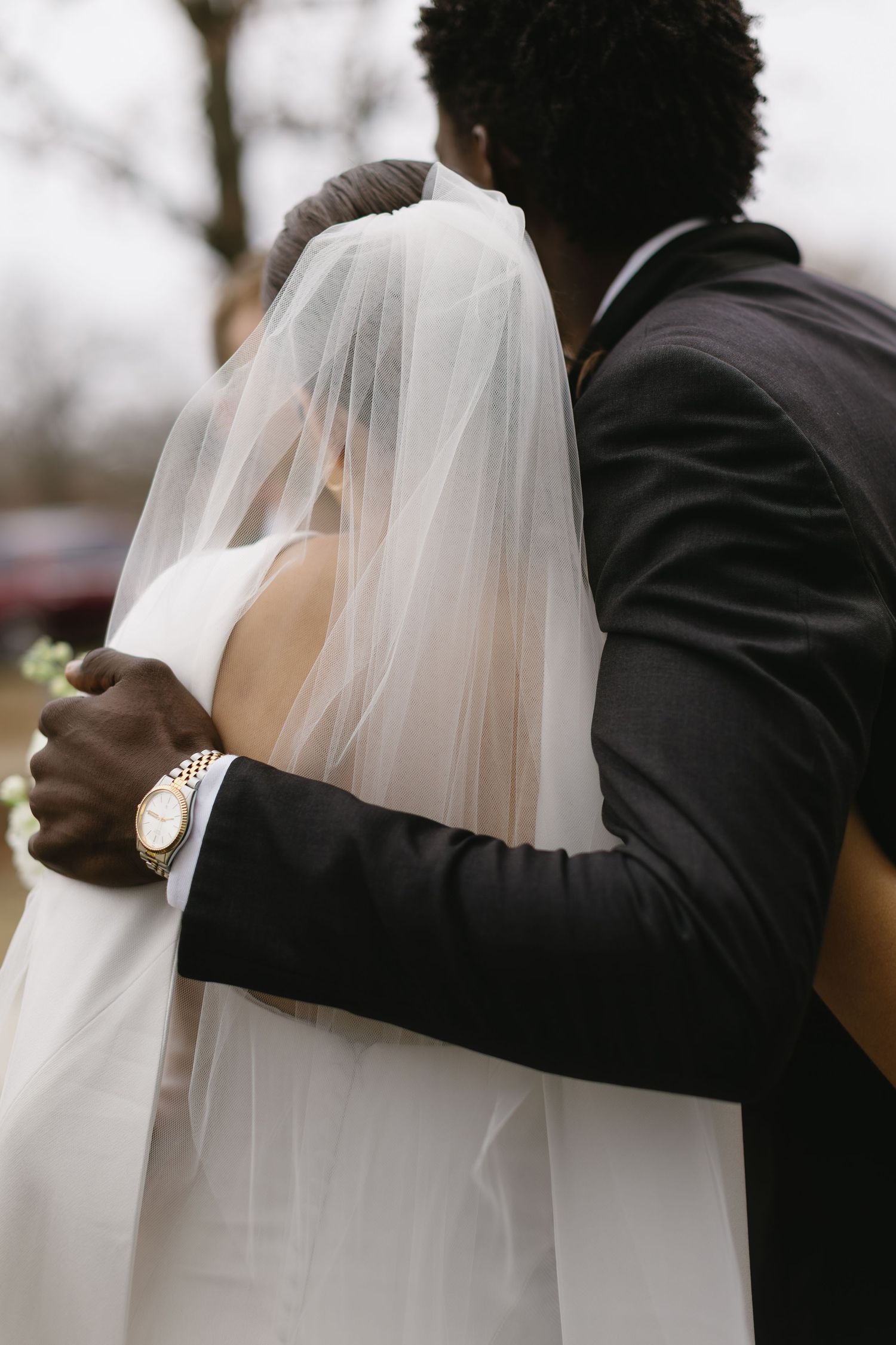 A tender embrace between newlyweds, focusing on the flowing white veil and formal attire.