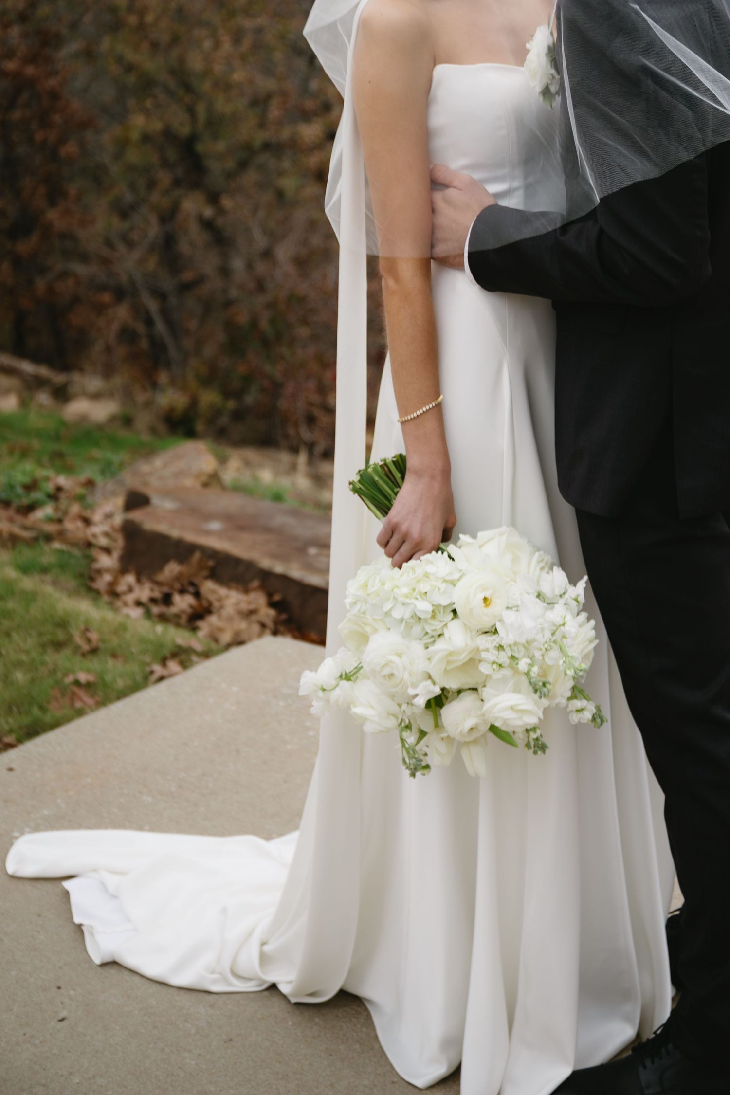 Elegant white wedding dress and bouquet detail shot showing flowing fabric and white floral arrangement.