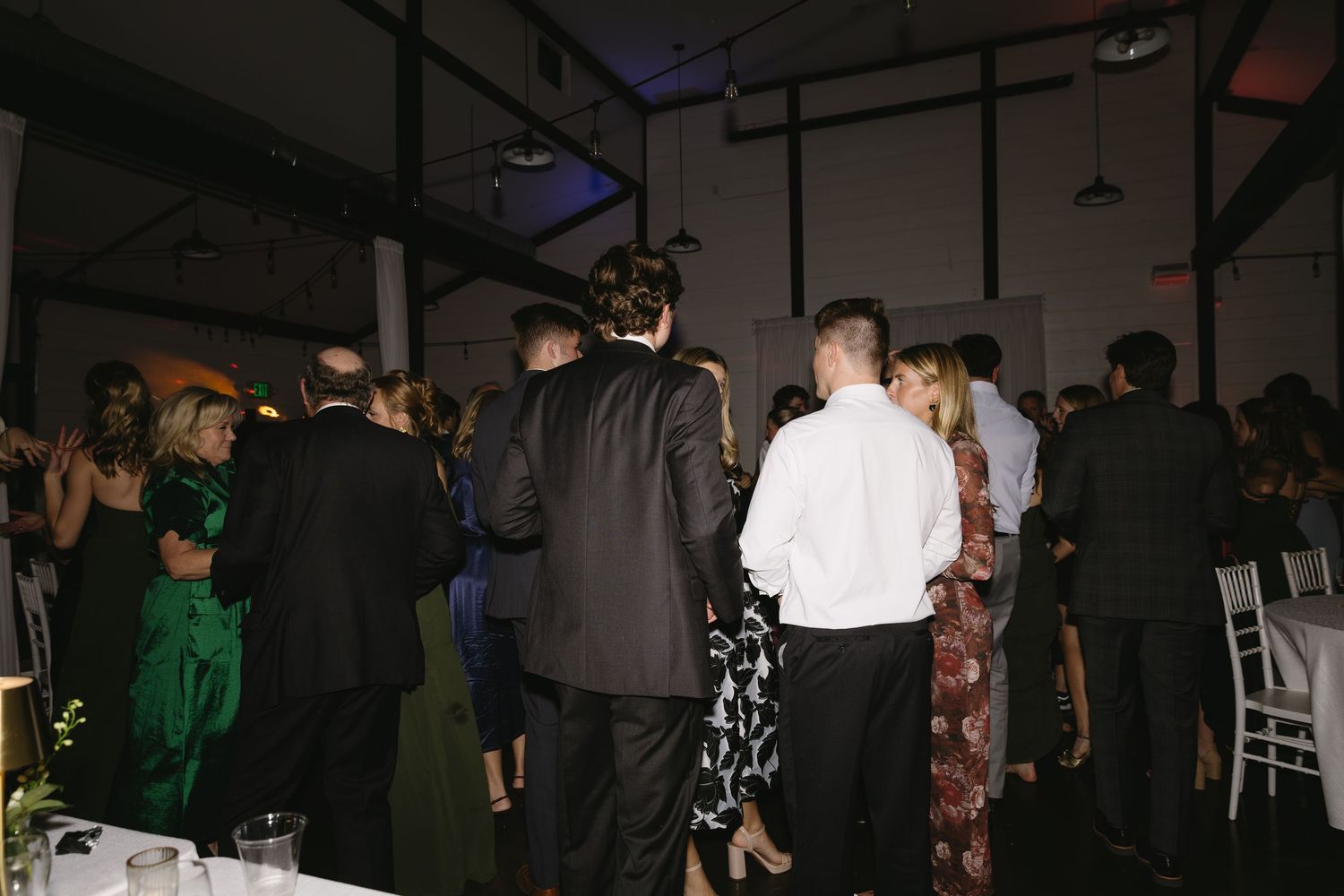 Dark reception venue filled with dancing wedding guests and ambient lighting.