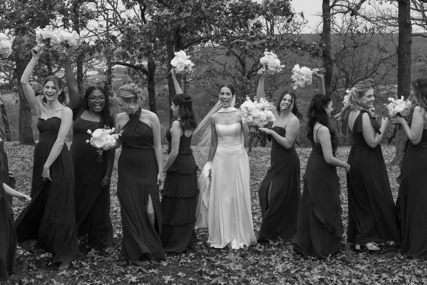 A black and white photo of a bridal party laughing together outdoors.