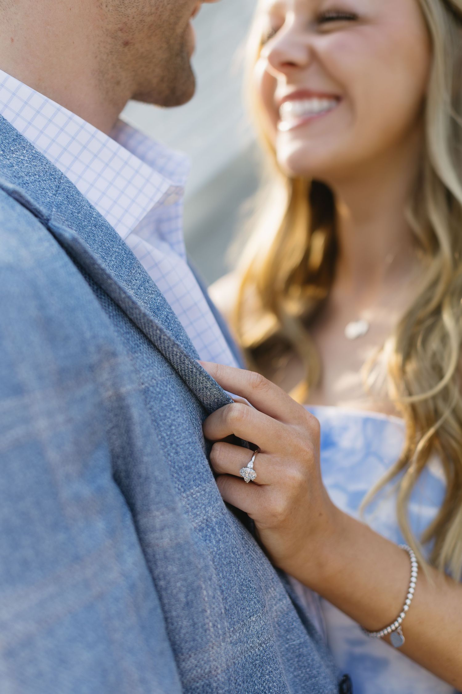 Close up of a joyful couple embracing with a sparkly diamond engagement ring visible on her hand.
