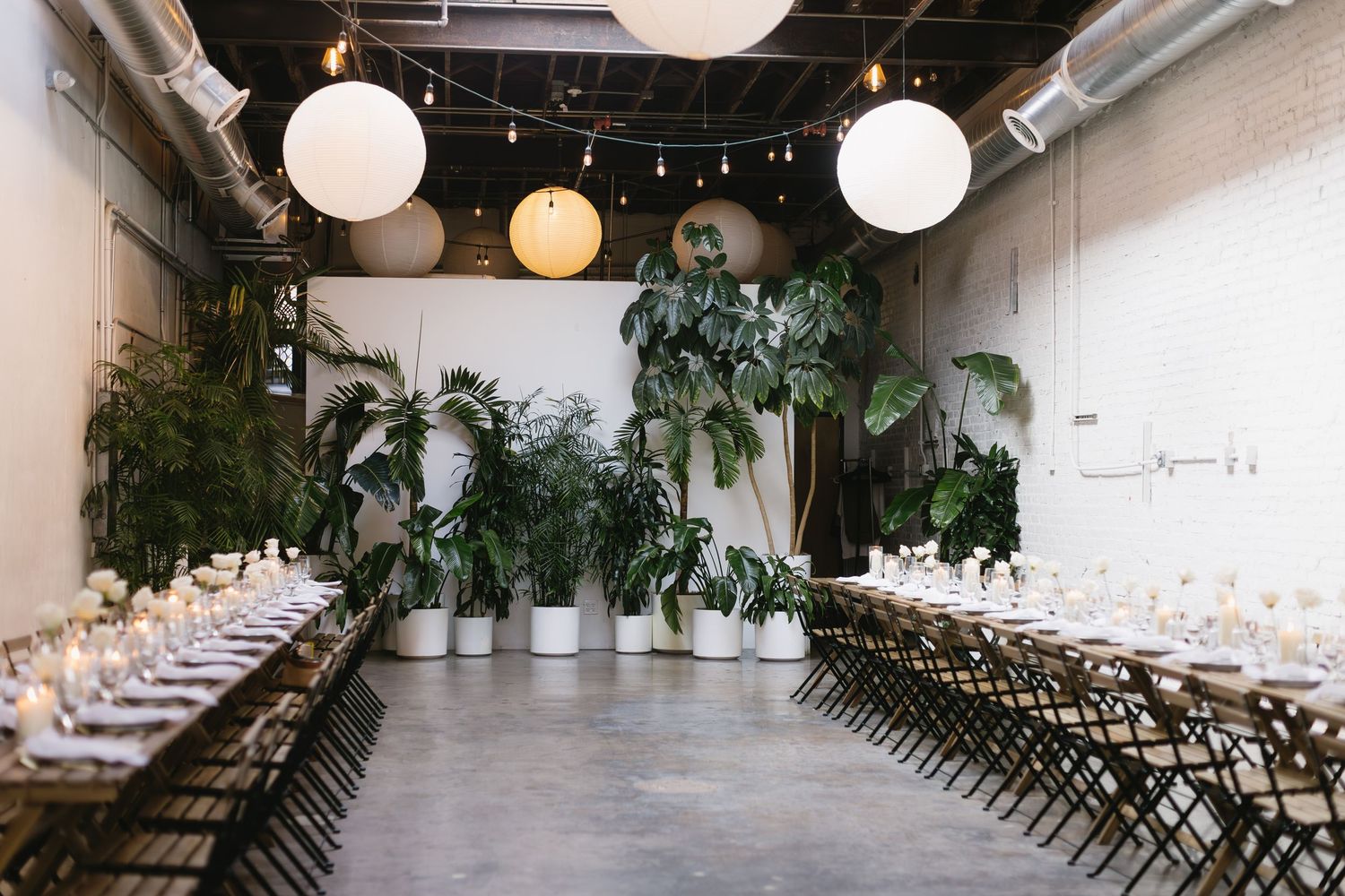 Modern indoor wedding venue with white walls, wooden chairs, and hanging paper lanterns creating an elegant atmosphere.