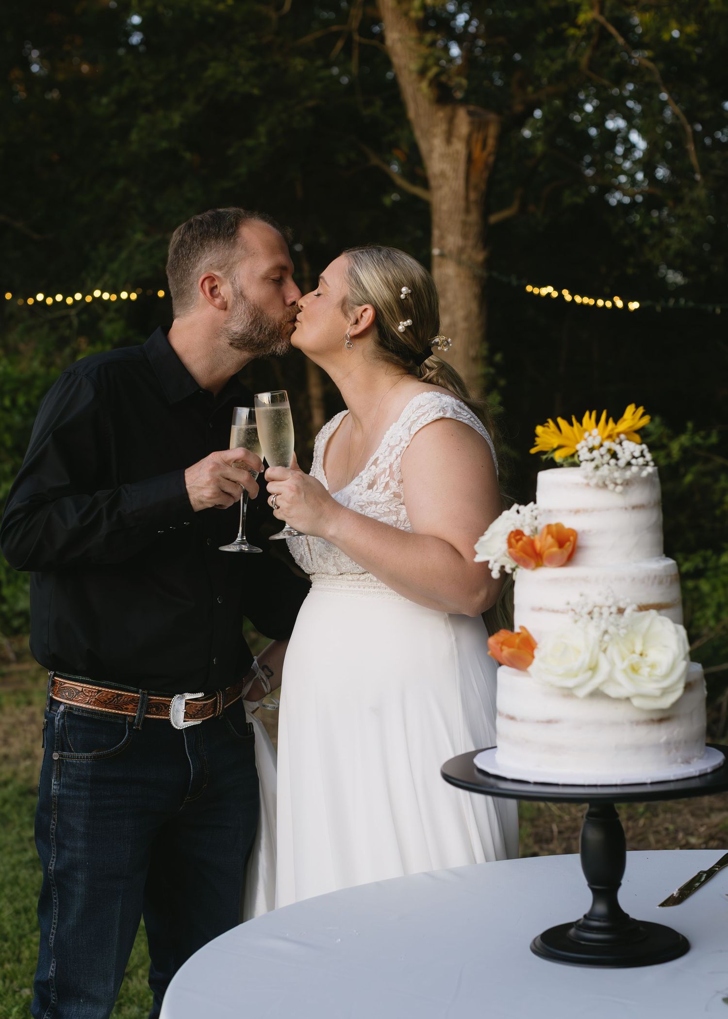 Wedding couple sharing intimate moment near white tiered cake decorated with sunflowers.