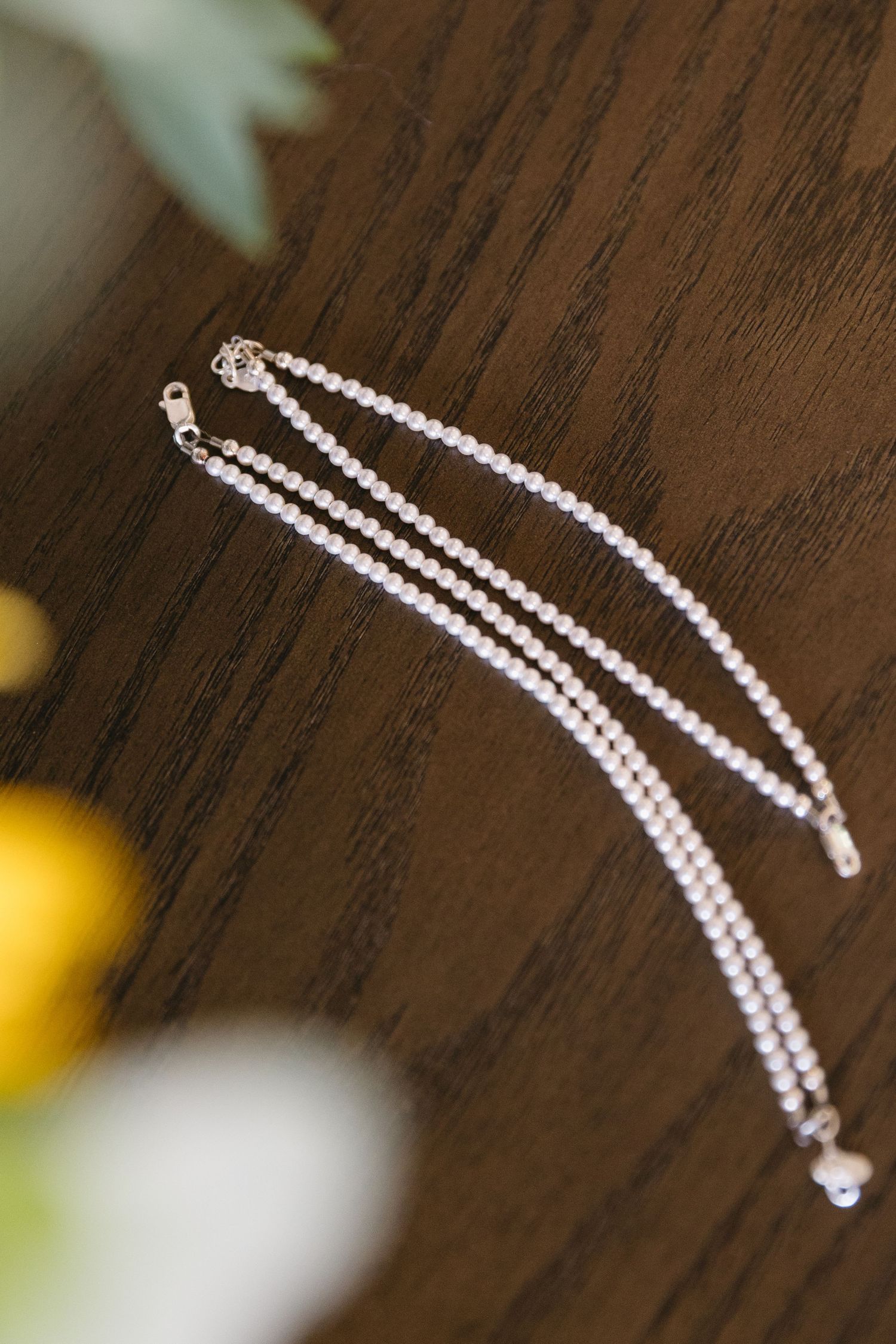 Delicate pearl necklace displayed on dark wooden surface with soft focus background.