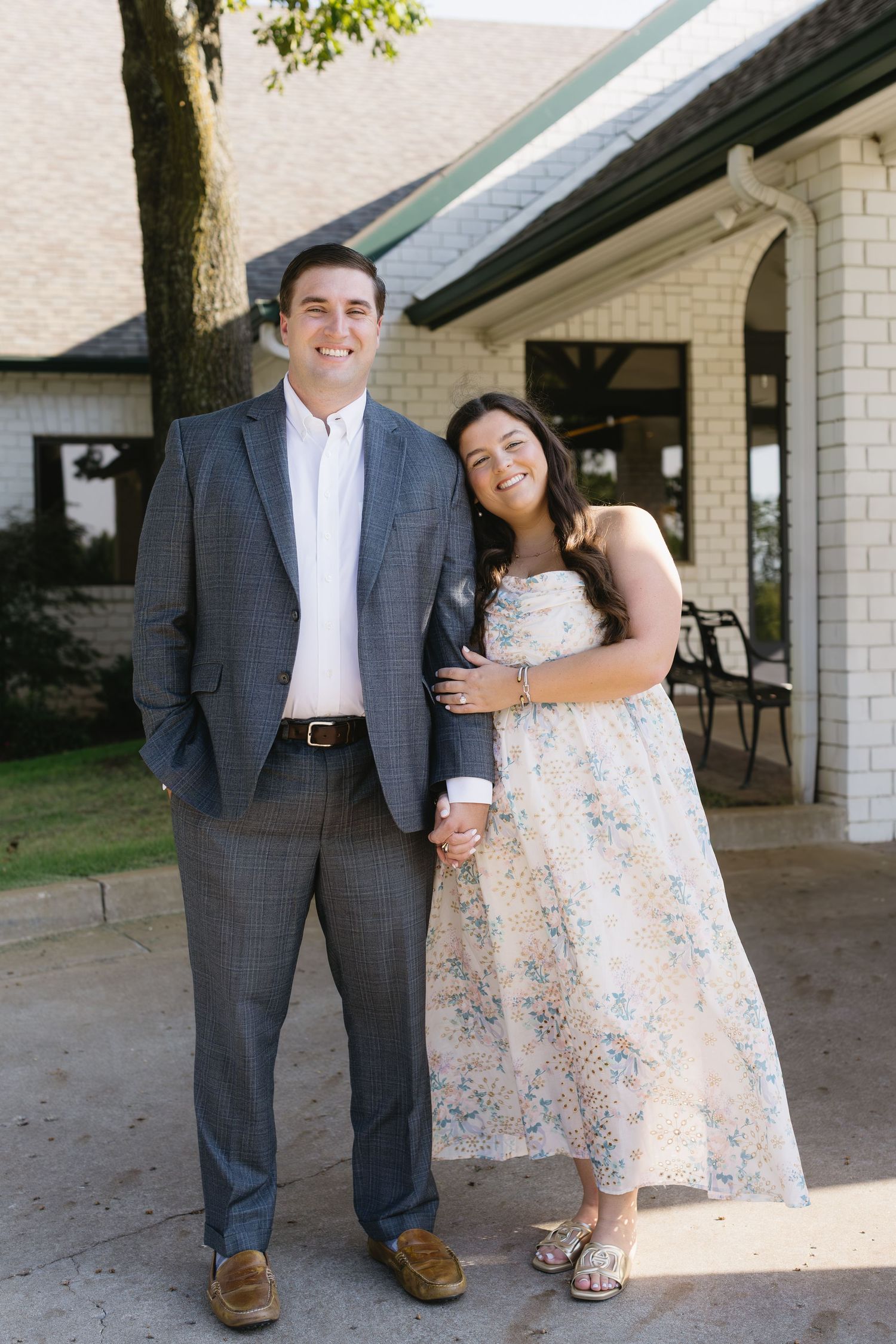 A couple in formal attire shares a joyful moment together outside a brick building.