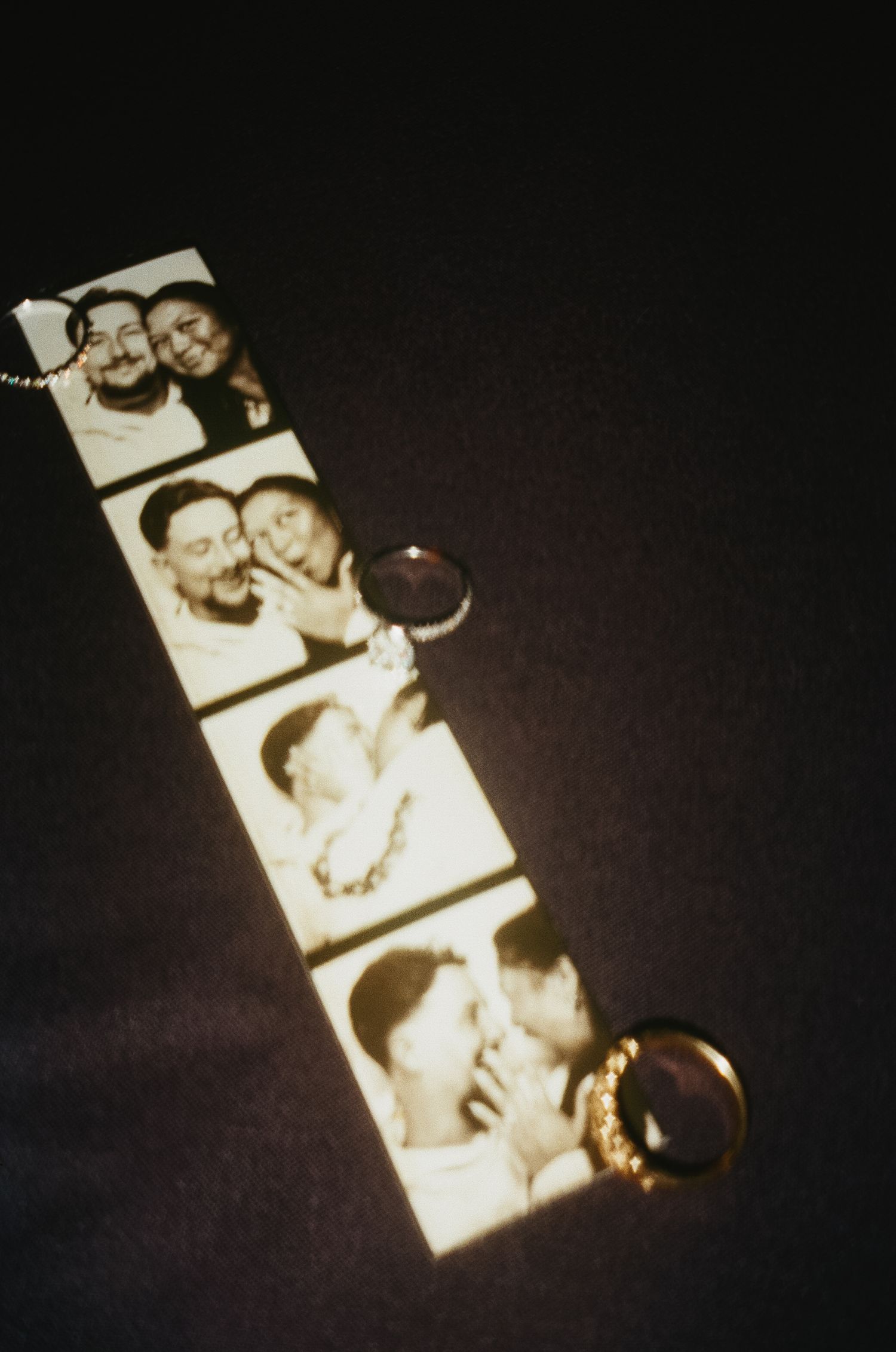 Vintage photo booth strip with wedding rings attached showing black and white snapshots.