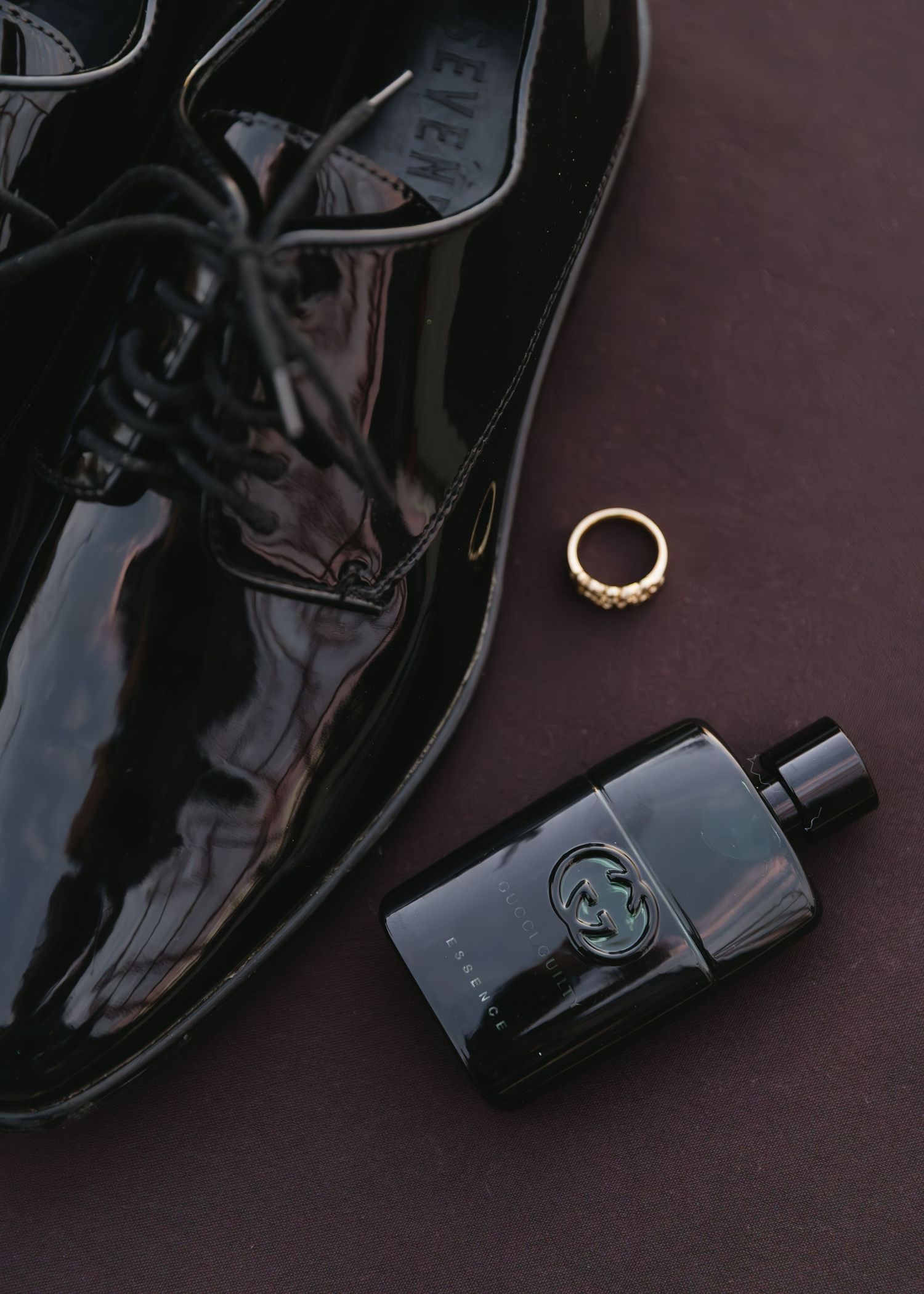 Wedding details featuring black patent leather shoes, gold ring and Gucci cologne bottle.