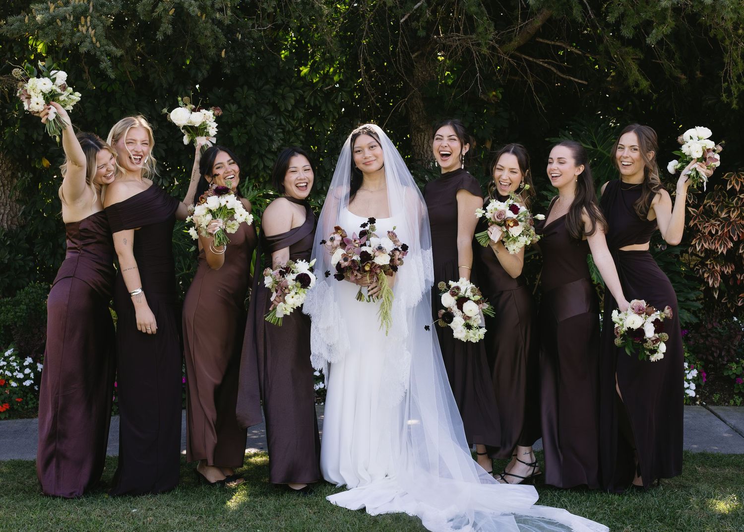 Wedding party in burgundy dresses poses with a bride in white for formal group photos.