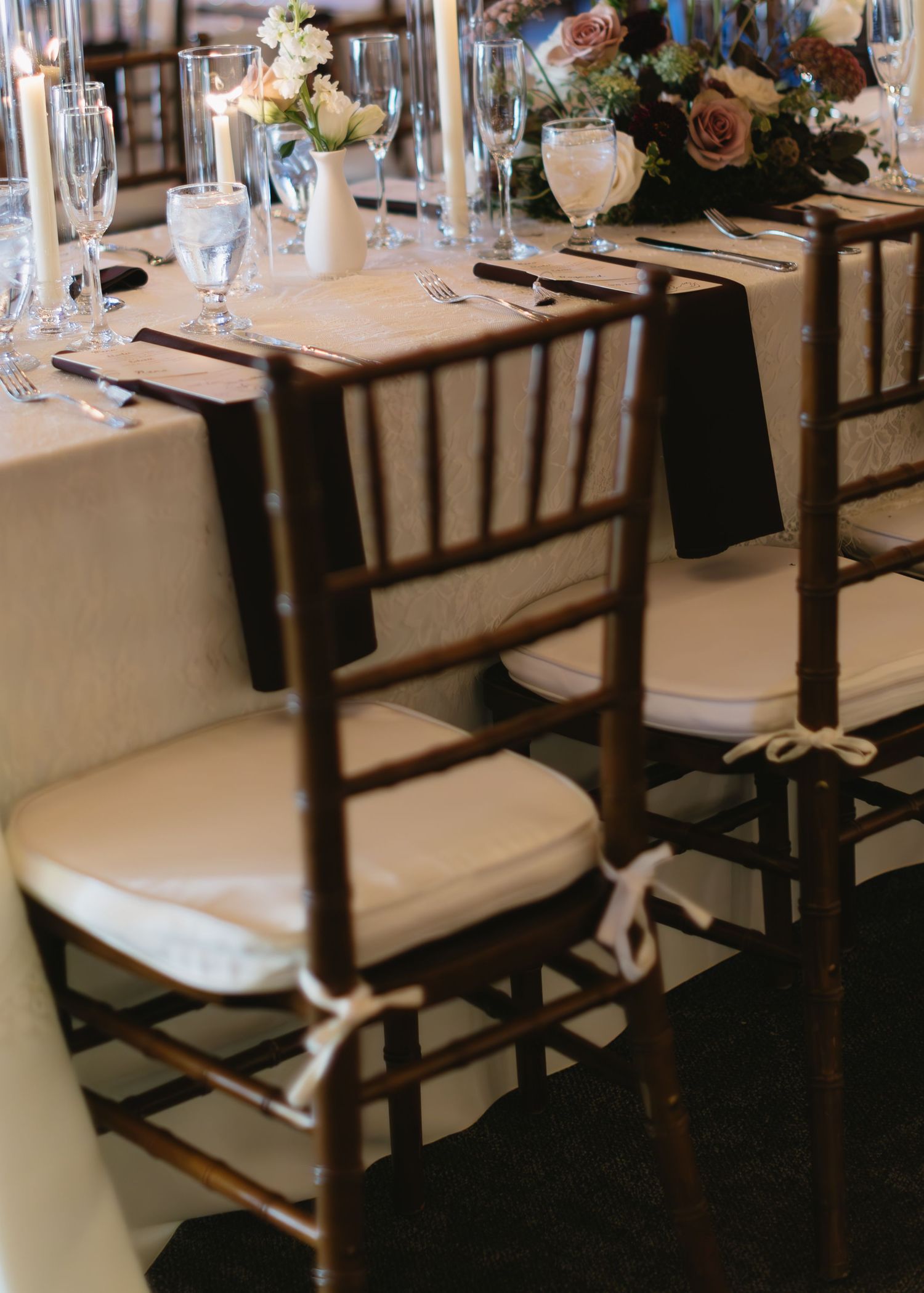 Elegant wedding reception table setup with dark wooden chairs and white cushions.