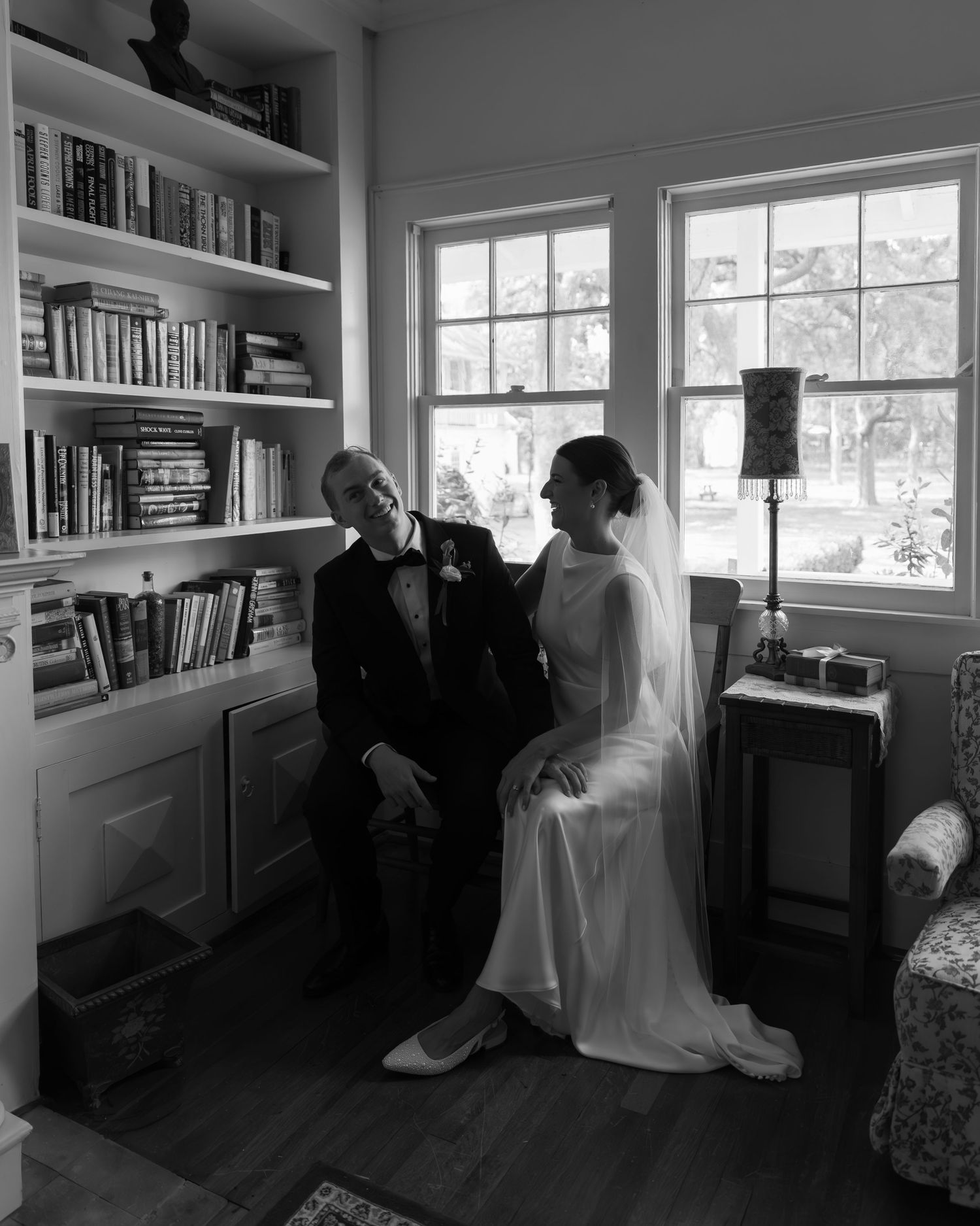A panoramic black and white photo showing figures sitting in a cozy library room with built-in bookshelves and windows.