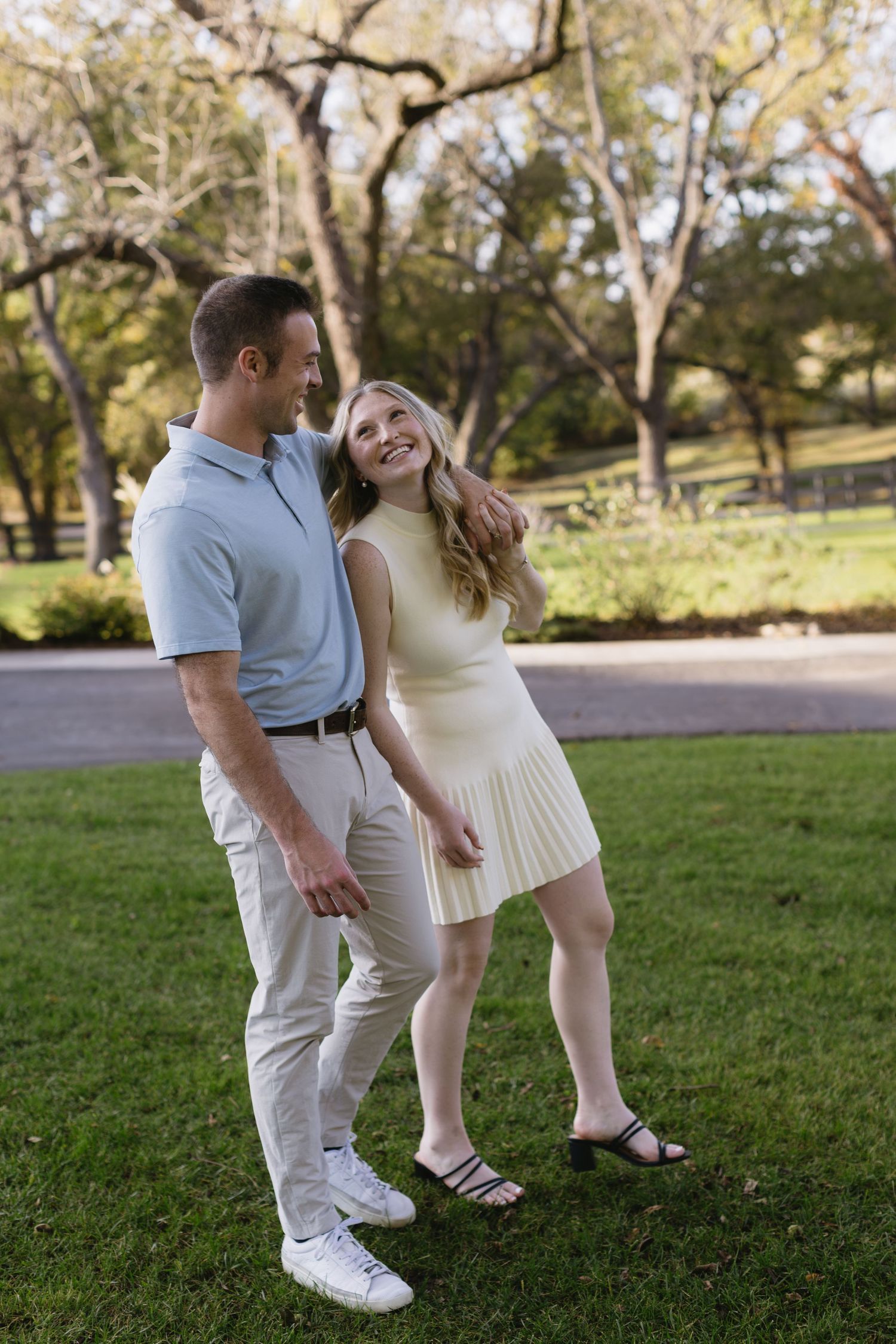 A couple shares a joyful moment together on a grassy lawn in a park setting during a sunny day.