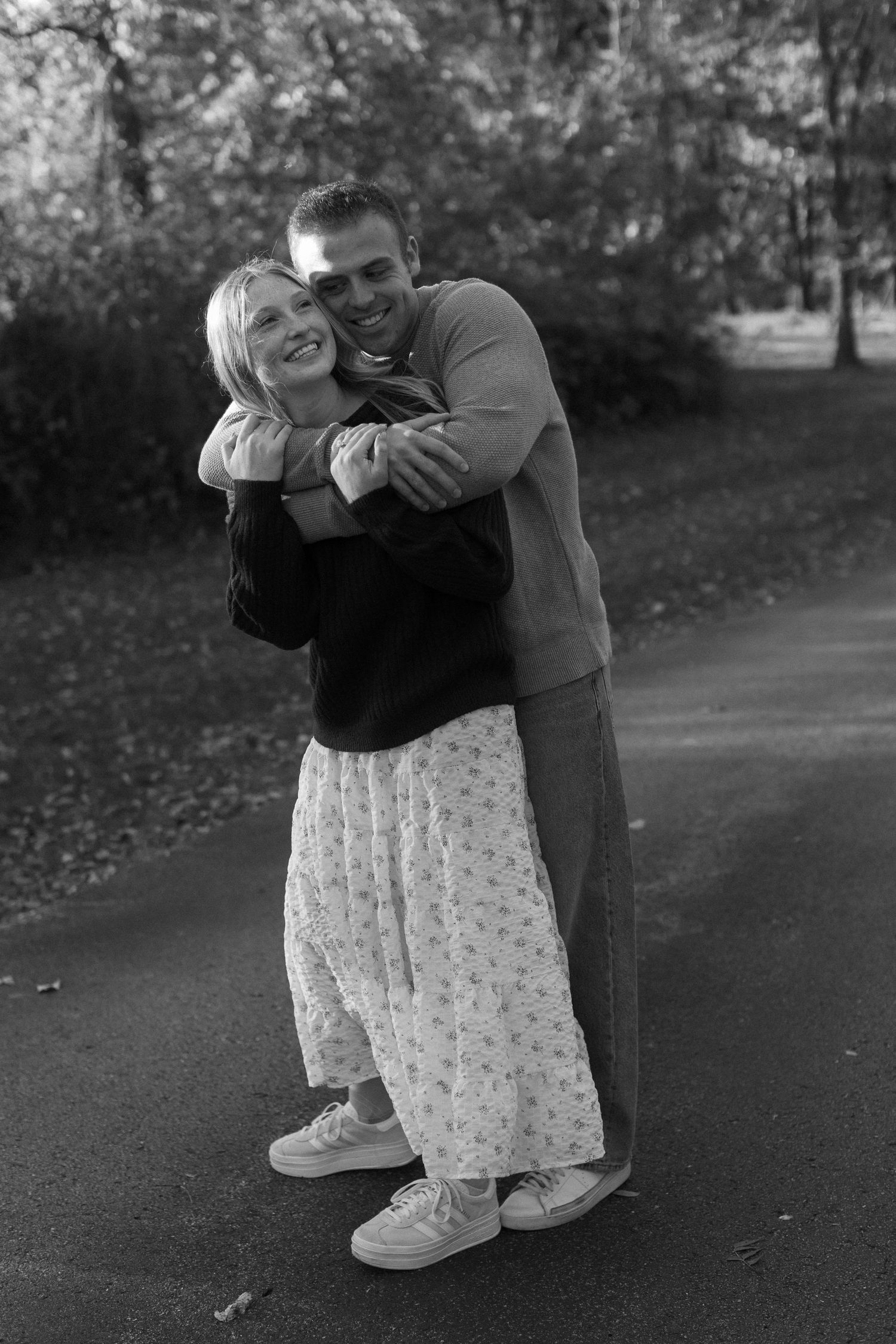 A sweet candid black and white photo captures a couple embracing and laughing together outdoors.