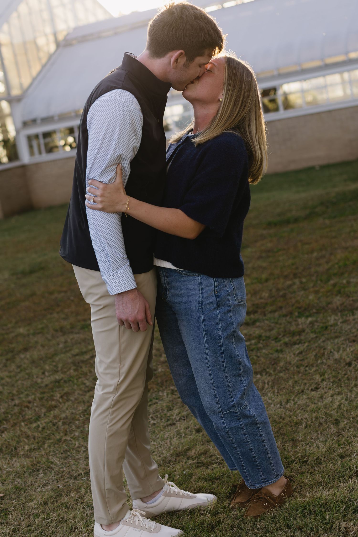 A couple embraces on a grassy lawn during a sunset photoshoot.