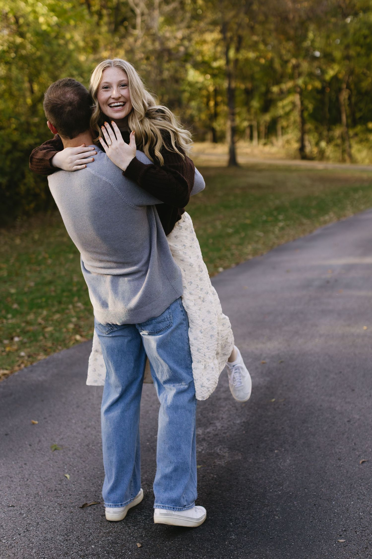 A playful couple spins and hugs on a paved park path.