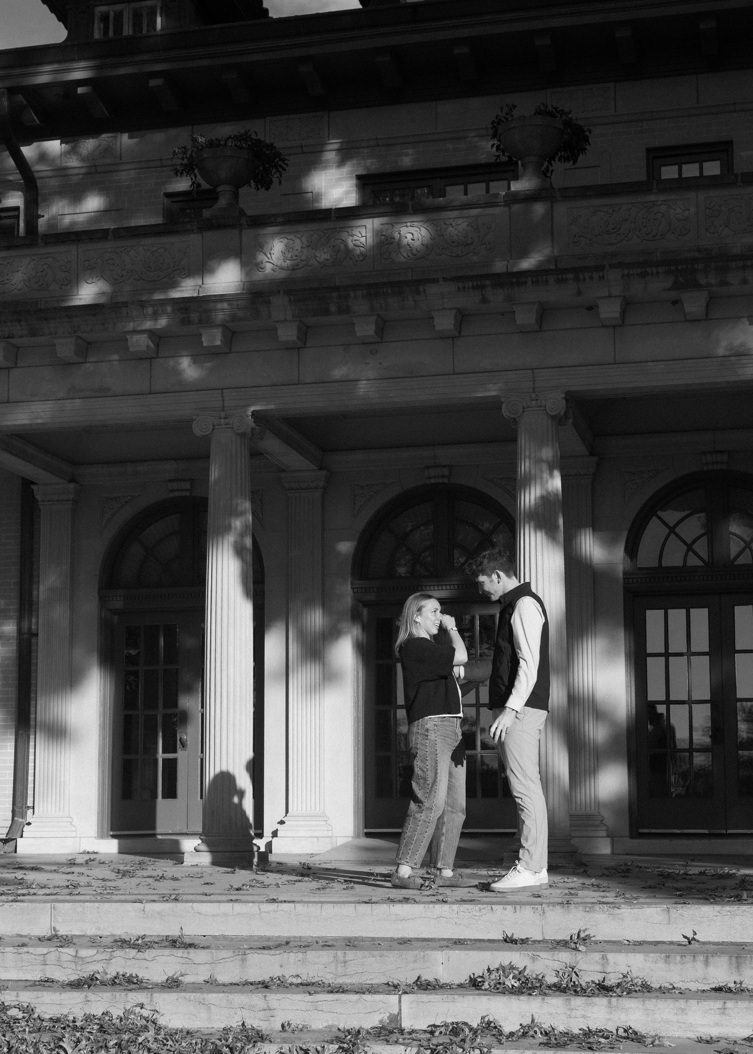 A black and white photo of people standing near a classical building with columns and arched windows.