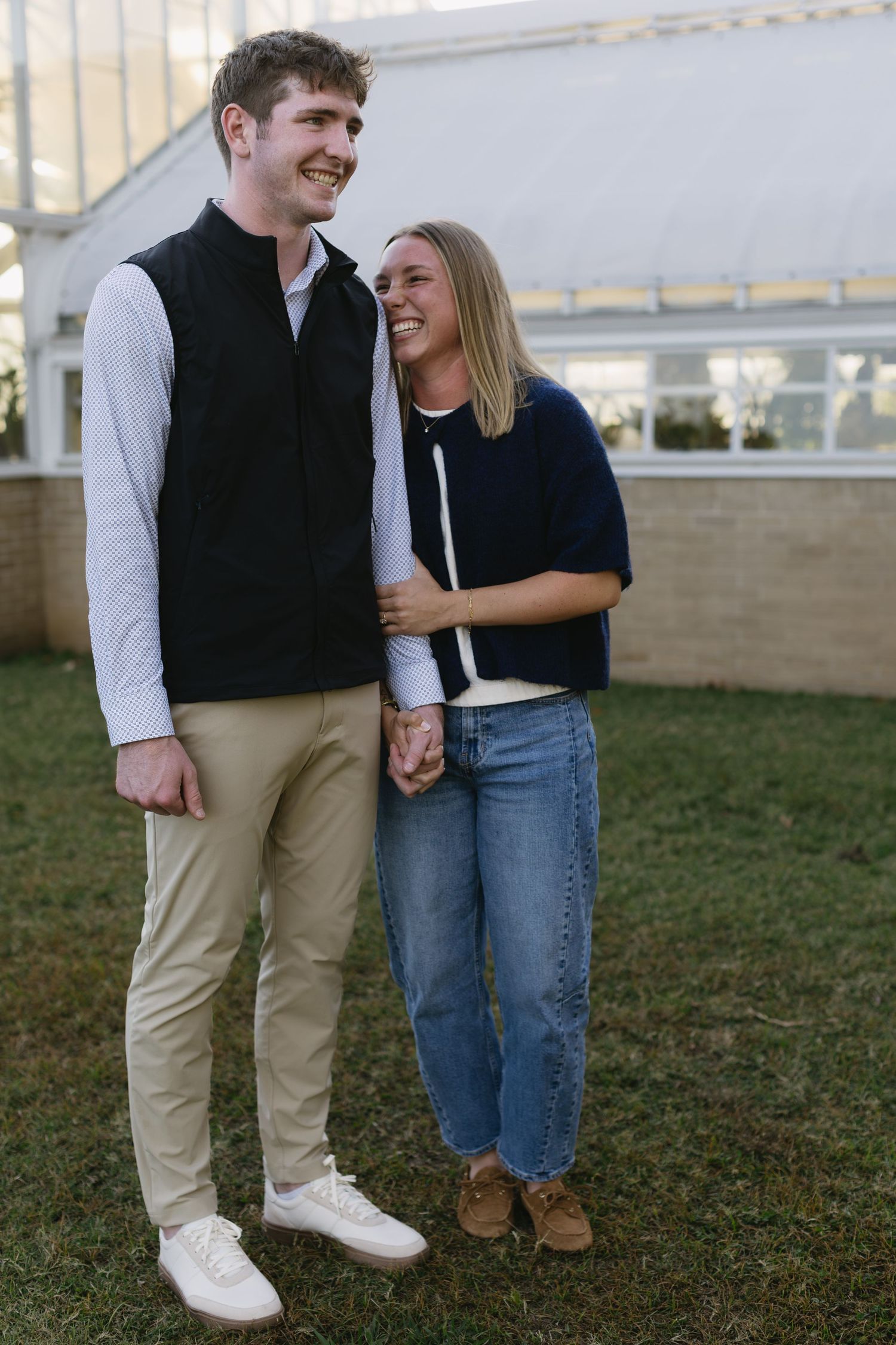 A couple shares a joyful moment together outdoors, wearing casual fall attire and holding hands.