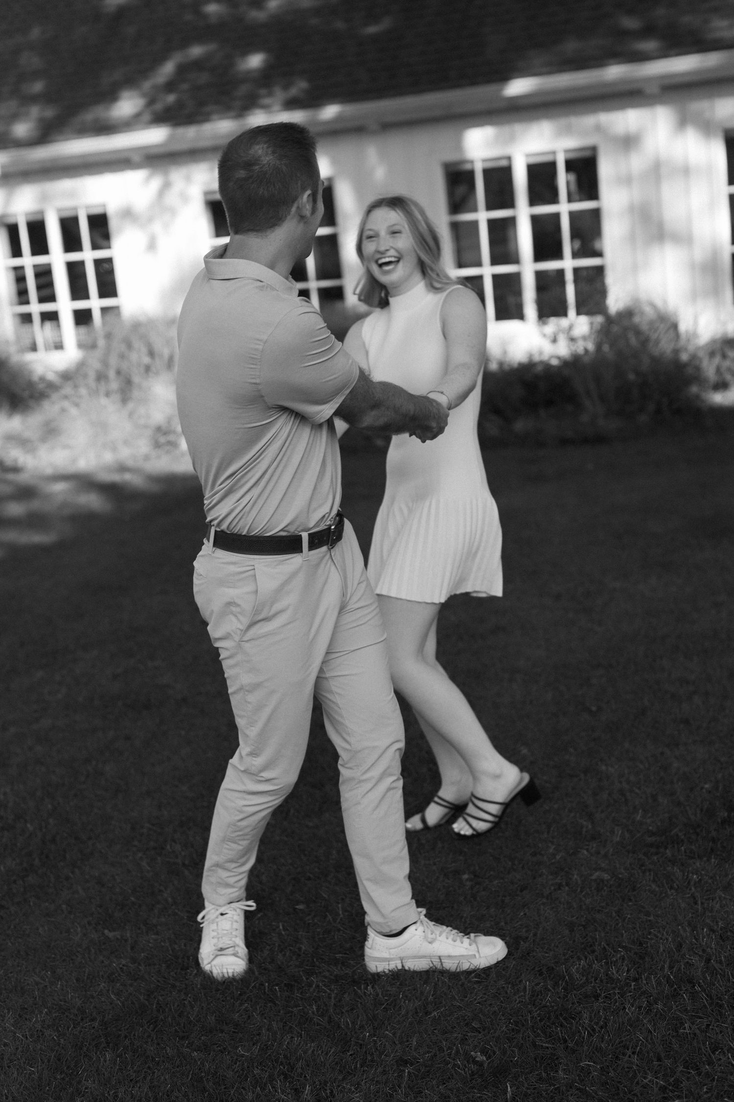 A couple dancing playfully together on grass in black and white photography.