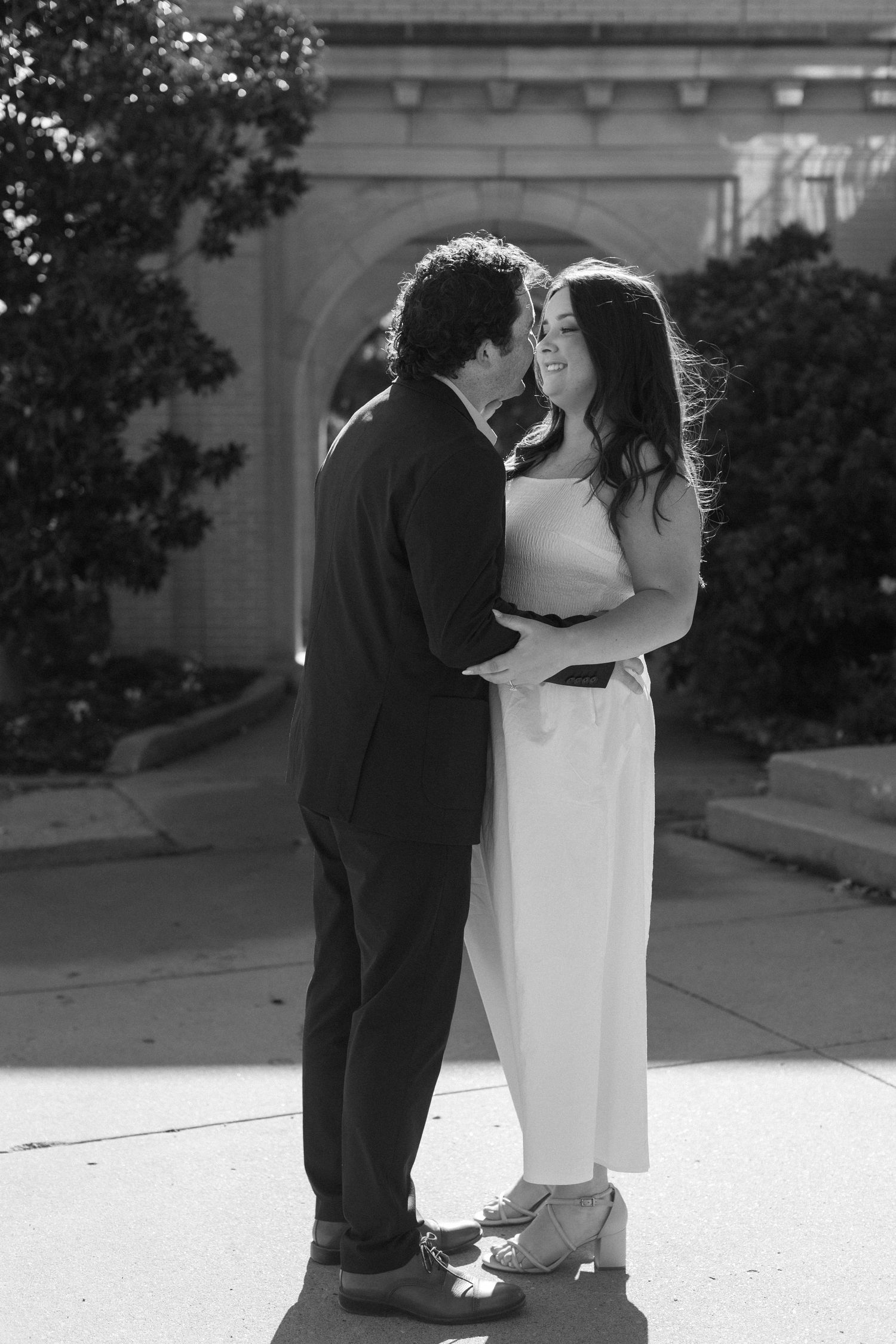 A black and white photo capturing a romantic moment between a couple in formal wear.