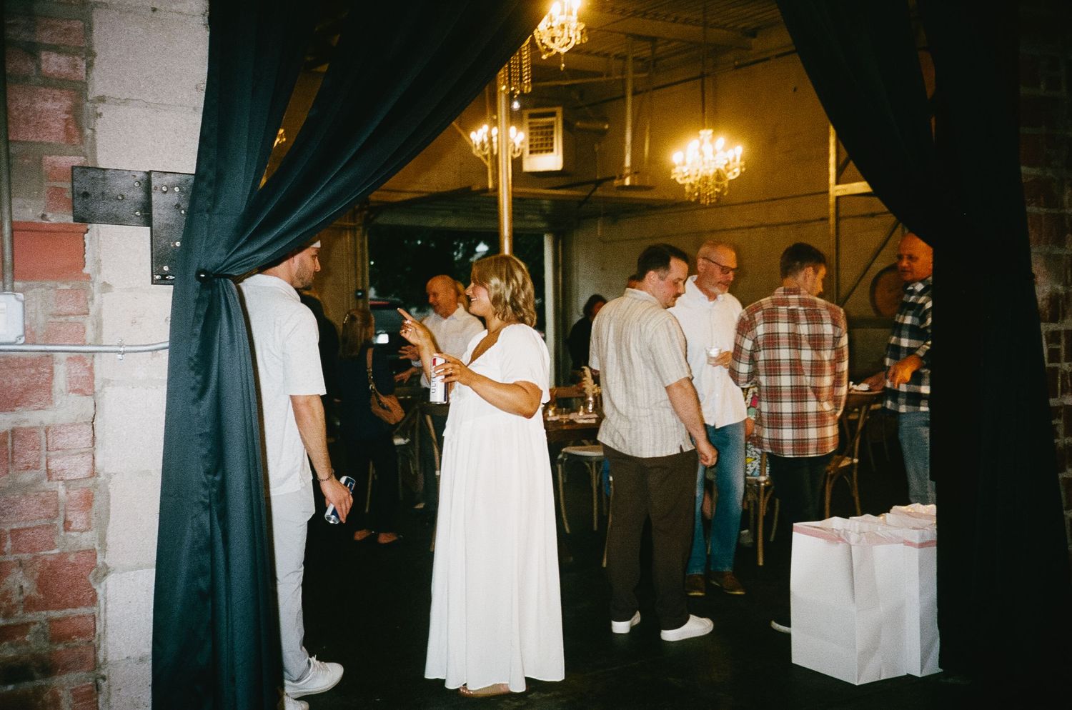 Wedding reception gathering with navy curtains and string lights in industrial space.