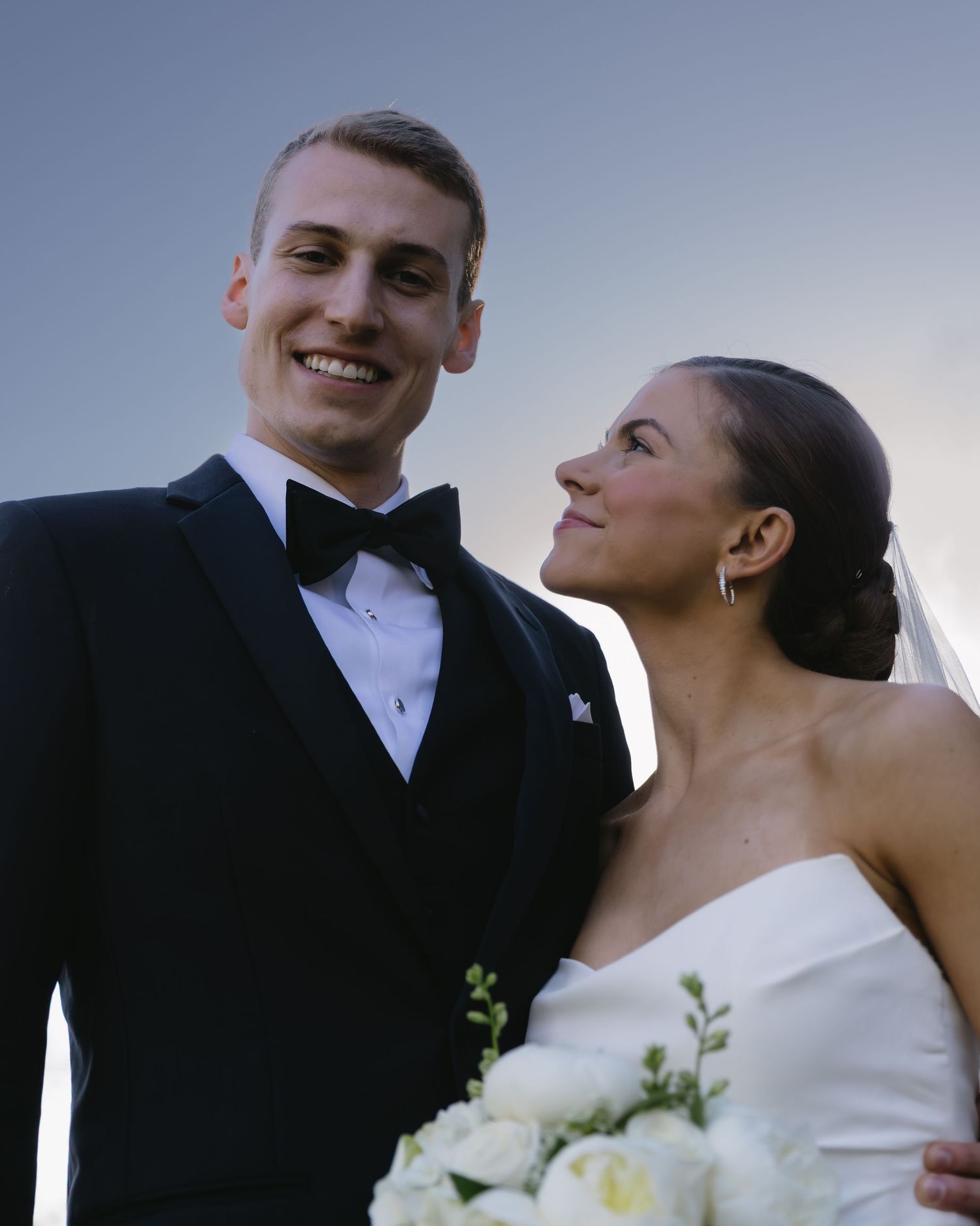 An elegant wedding portrait taken at dusk with soft lighting and white floral bouquet.