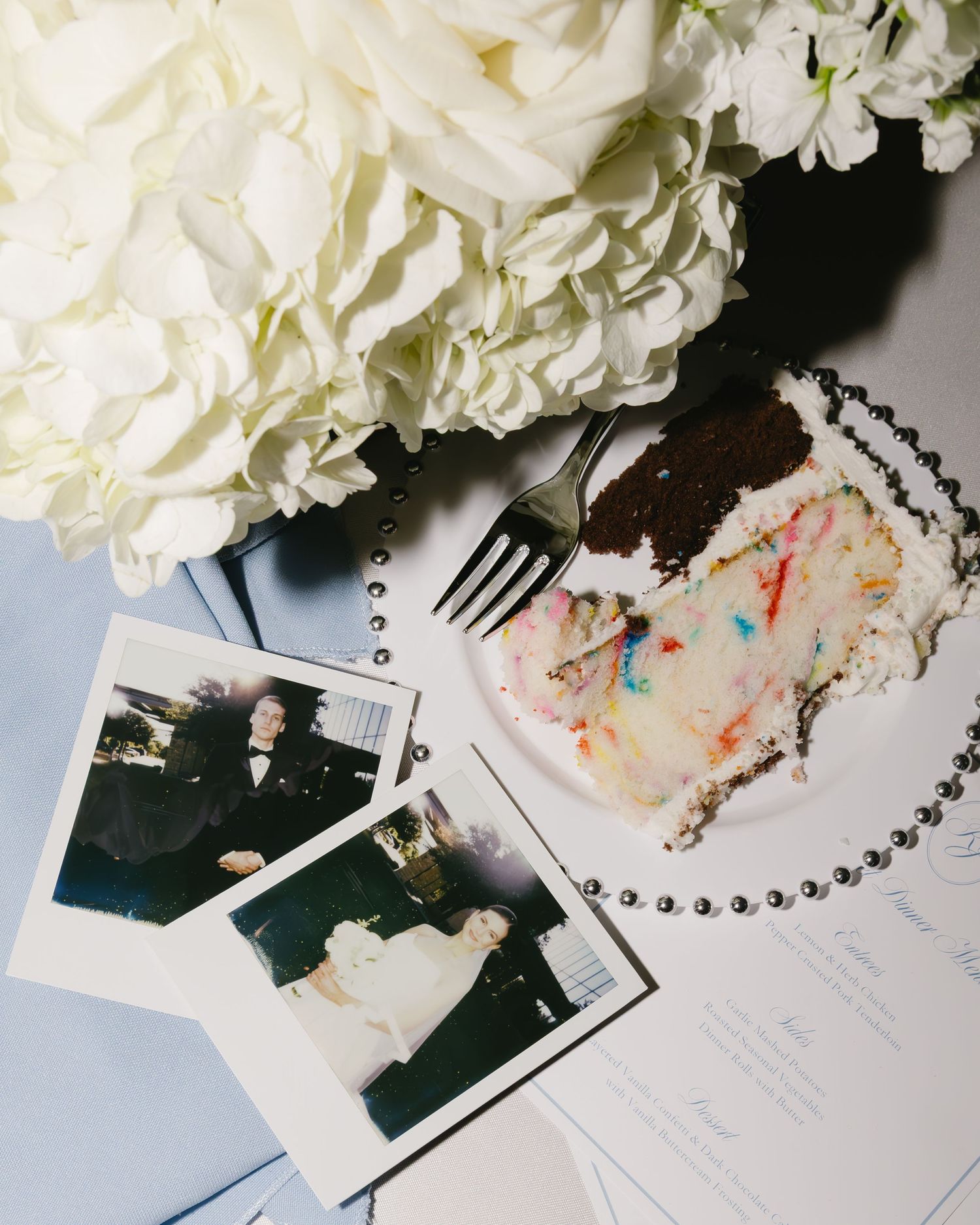 Wedding reception details with white hydrangeas and scattered polaroid photos.