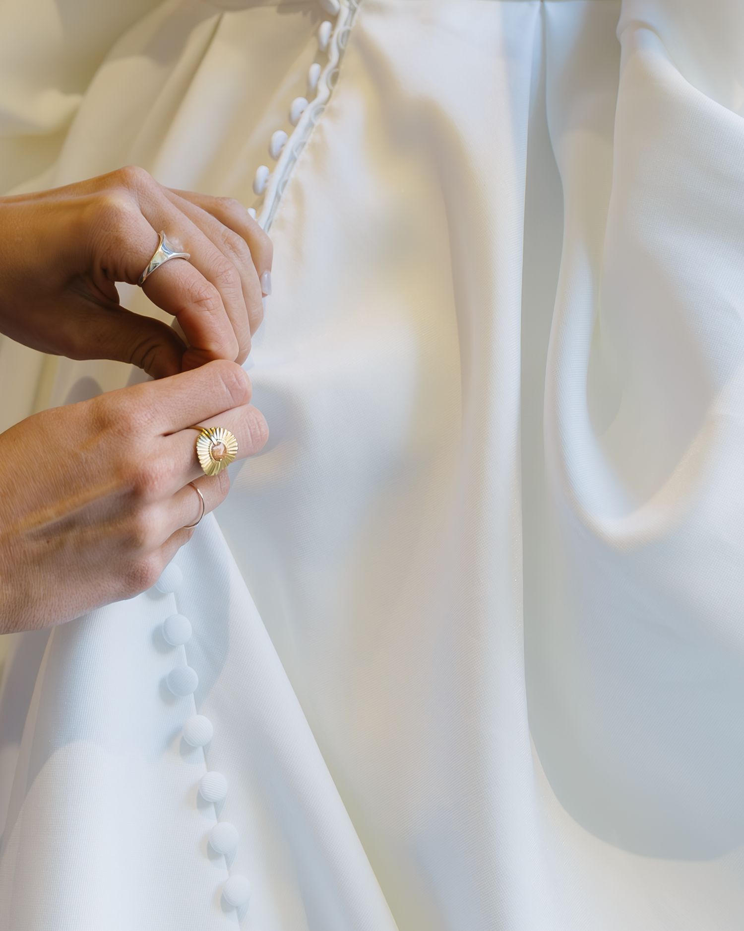 A row of close-up photos showing hands buttoning up a white wedding dress with delicate buttons and fabric details.