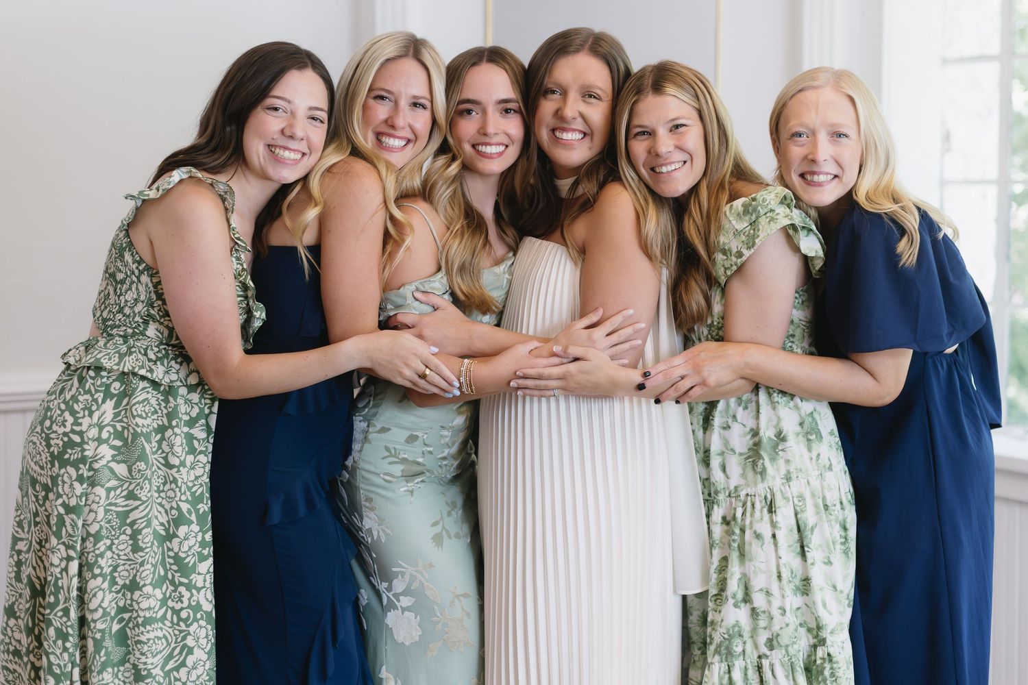 Row of bridesmaids wearing navy blue and floral print dresses posing together indoors.