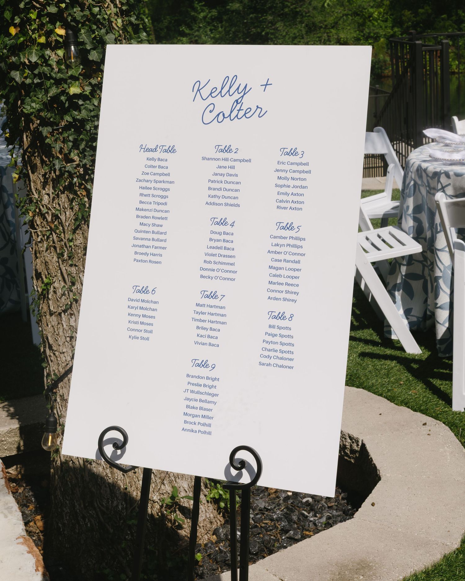 Wedding seating chart display showing table assignments in blue text on white board.