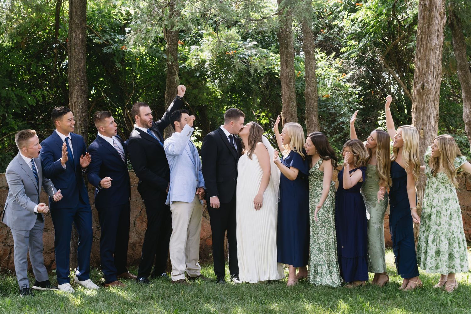 Wedding guests gathered in an outdoor setting, standing in a row among trees.