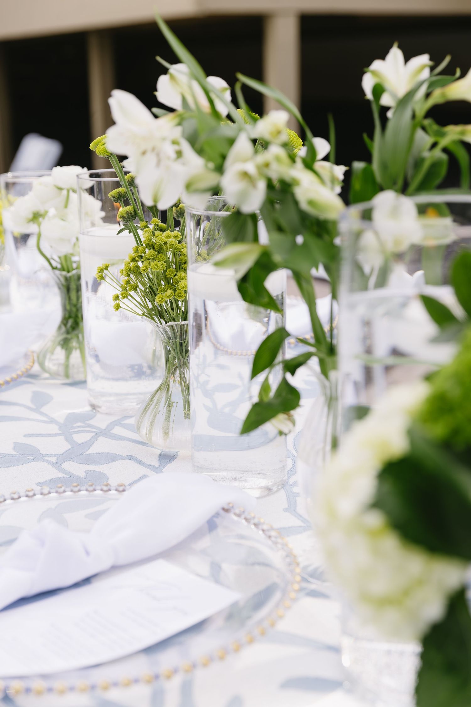White floral centerpieces in glass vases on elegant table settings with delicate blue accents.