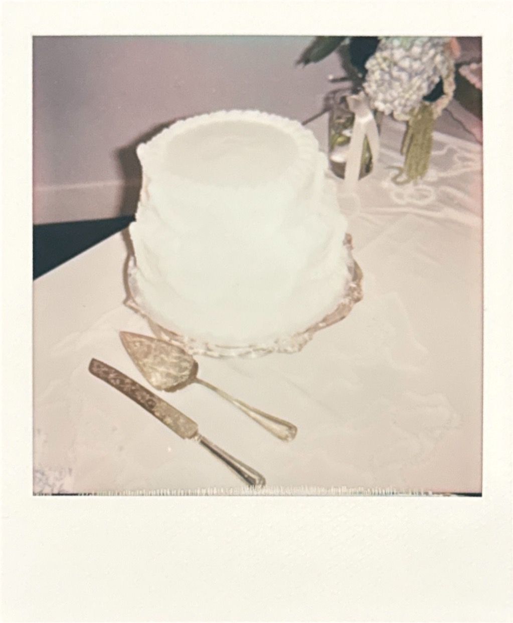 Traditional white wedding cake with delicate decorative details on plain tablecloth.