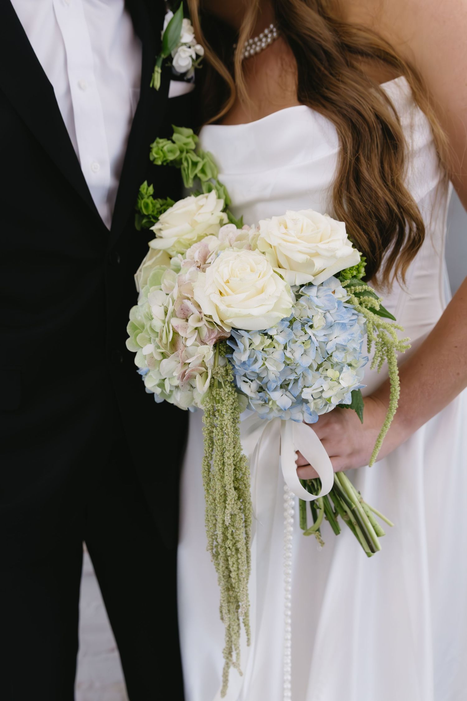 An elegant wedding bouquet with white roses, blue hydrangeas and cascading greenery.