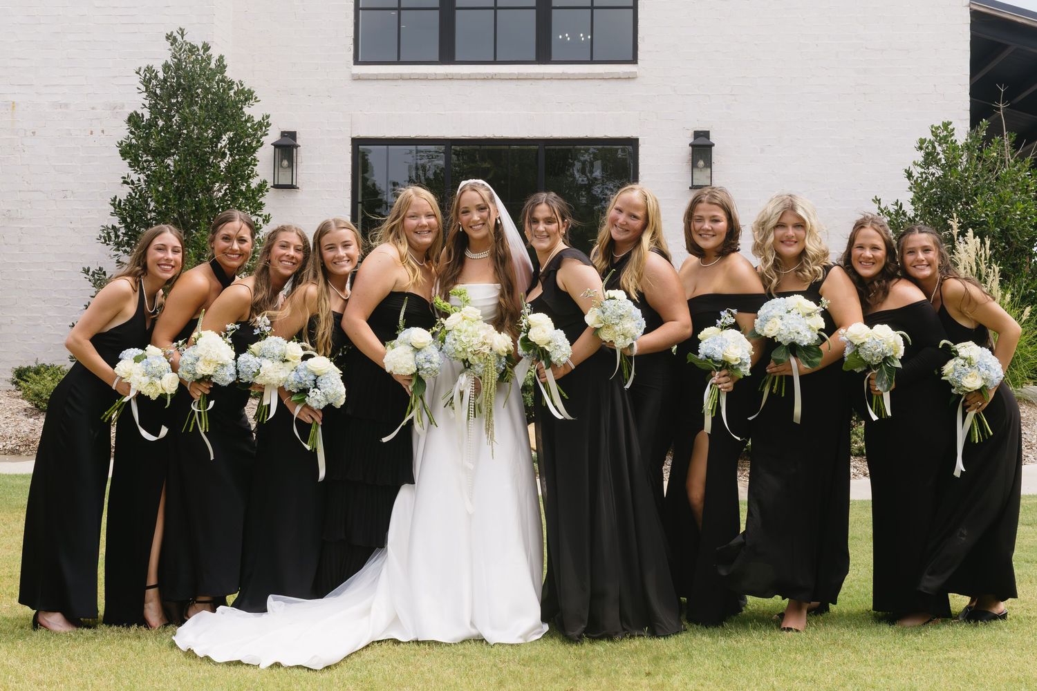Group photo of wedding party laying on grass with bridesmaids in black dresses.