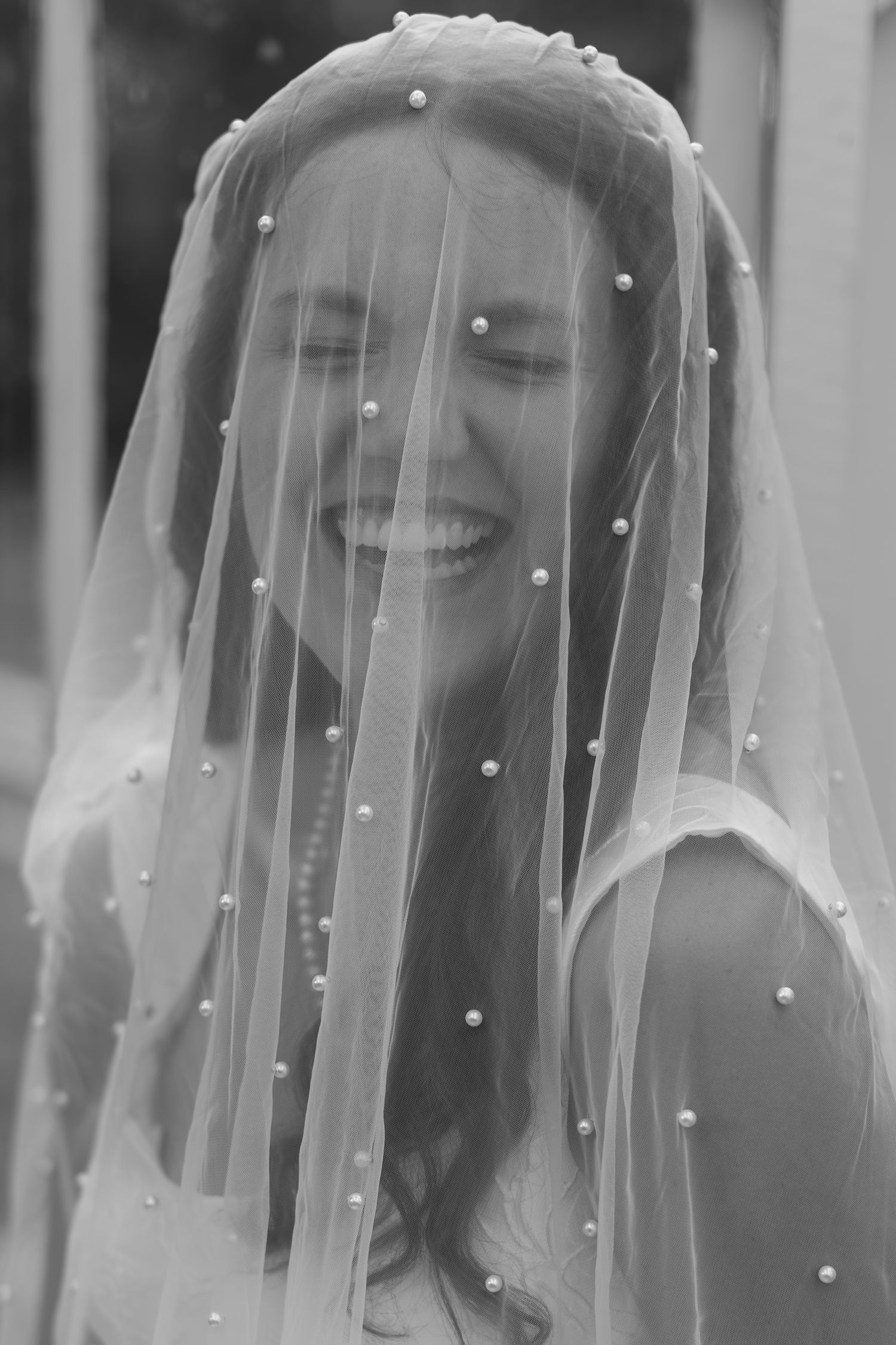 A joyful black and white portrait under a delicate pearl-dotted bridal veil.