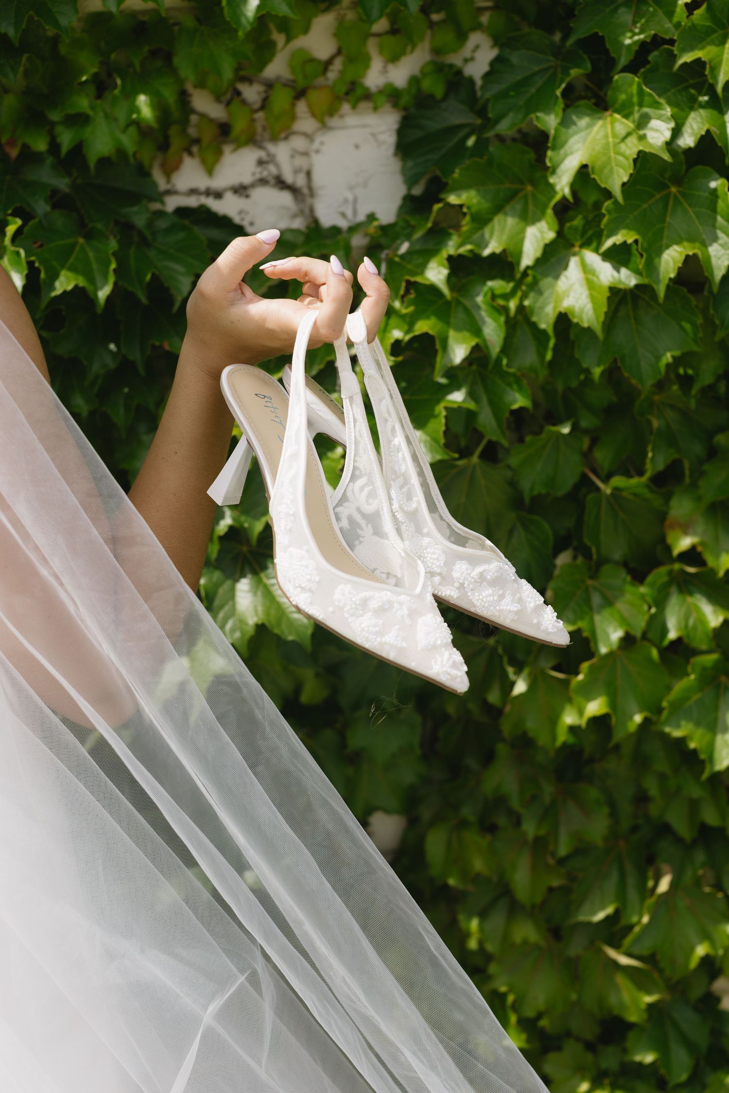 Close-up series of white bridal veil flowing in front of green ivy leaves backdrop.