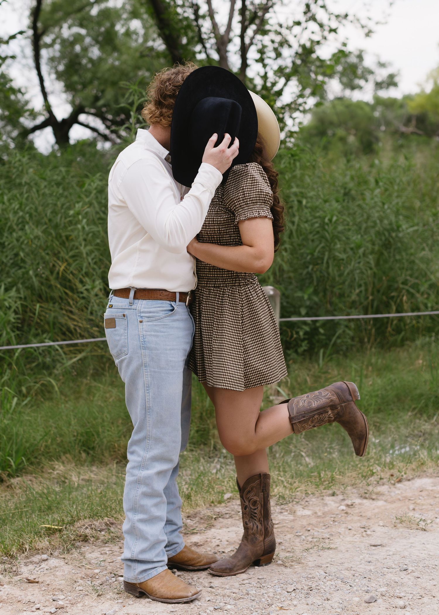 Couple's feet showing cowboy boots standing close together on a dirt path surrounded by green grass.