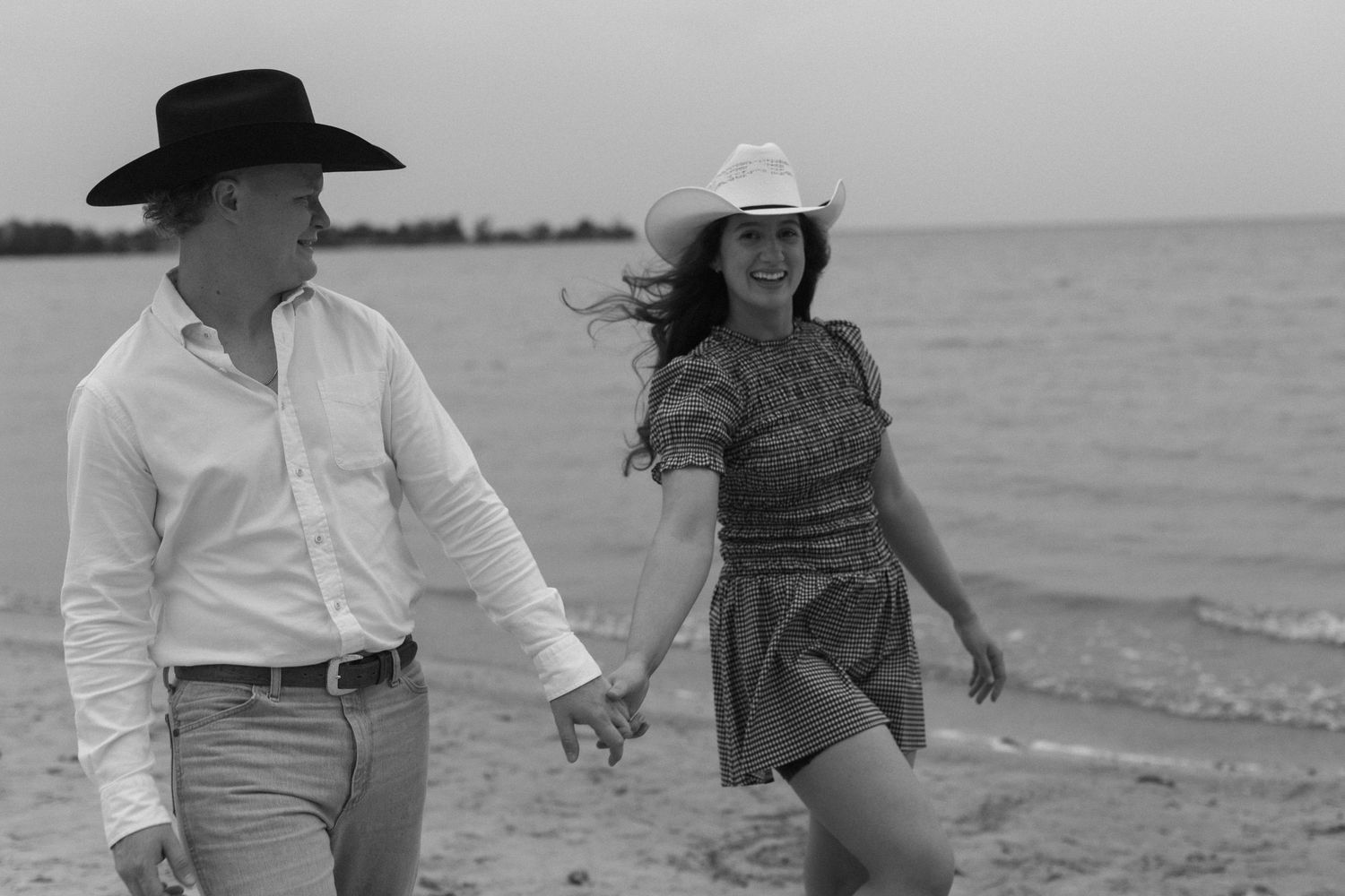 Black and white photo of couple walking hand in hand along the beach.