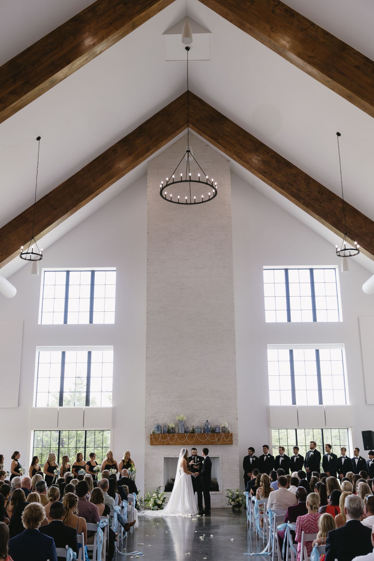 An elegant white chapel wedding ceremony with vaulted ceilings, exposed beams, and crystal chandeliers.