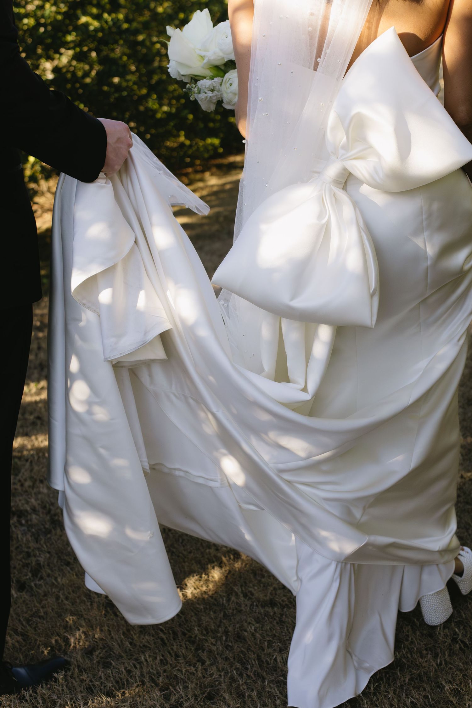 Close-up details of an elegant white wedding dress with dramatic folds and fabric texture in natural light.