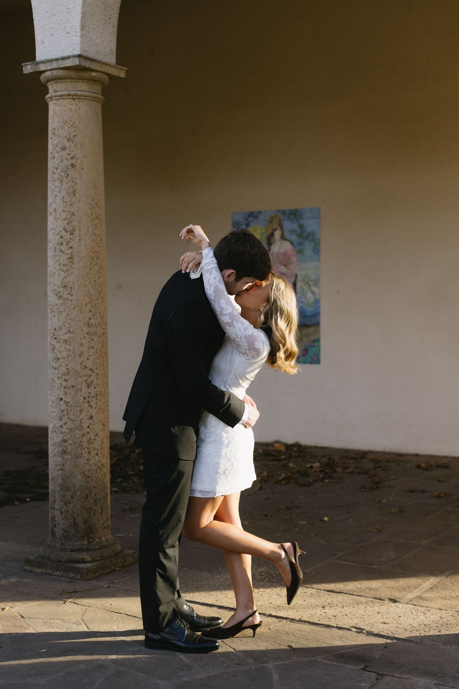 A romantic couple embraces near a stone pillar in warm lighting.