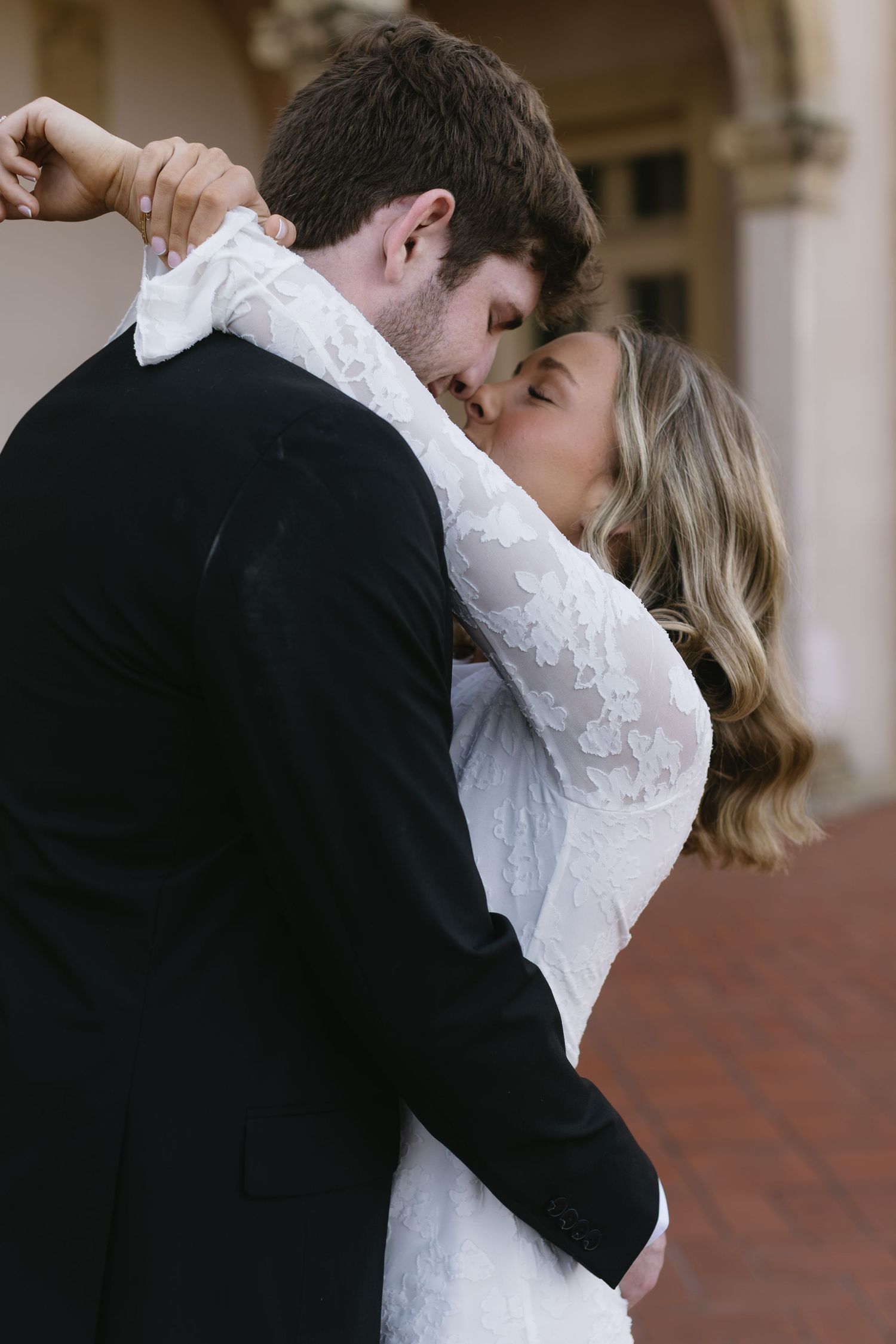 A romantic embrace captured in an ornate architectural setting with arched columns and warm lighting.