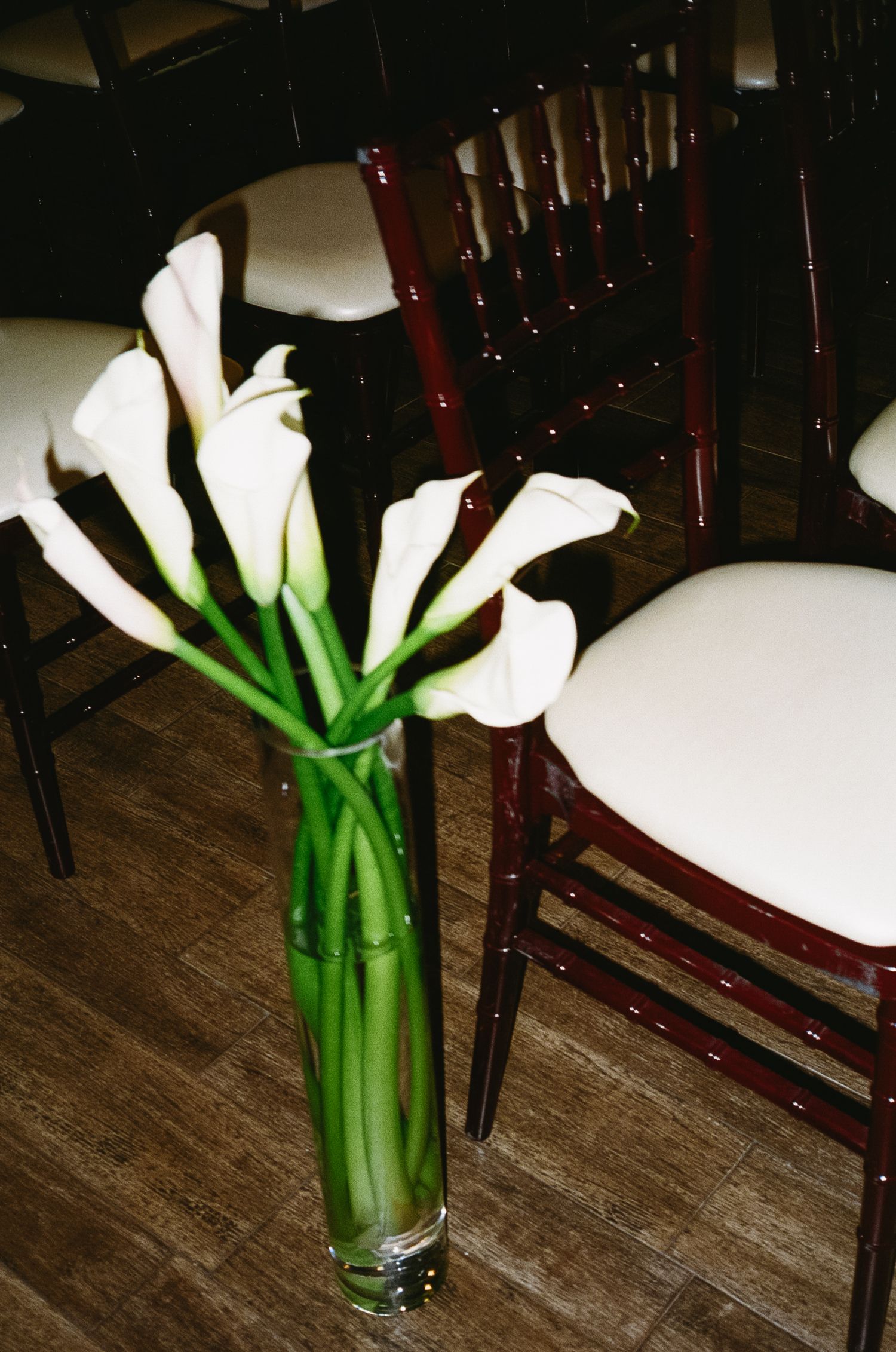 A collection of white calla lilies with long green stems arranged in a clear glass vase on a wooden surface.