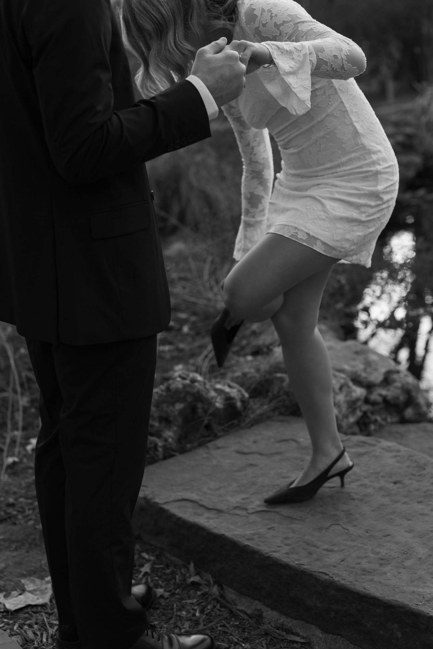 A couple in formal wear poses on stone steps during an artistic black and white photo session.