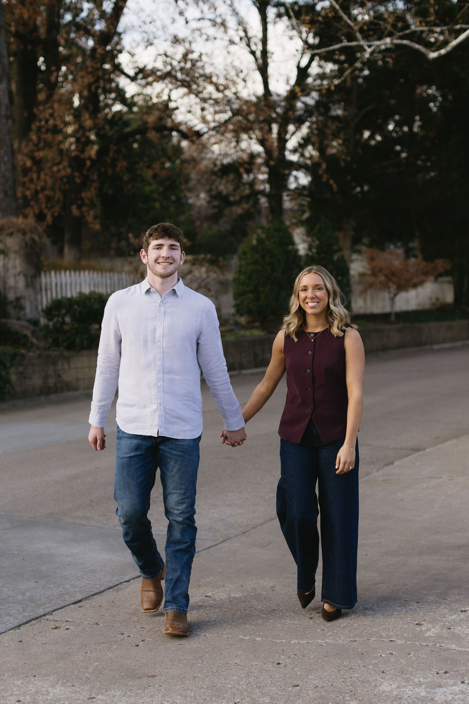 A couple walks together holding hands on a path during an outdoor engagement photo session.