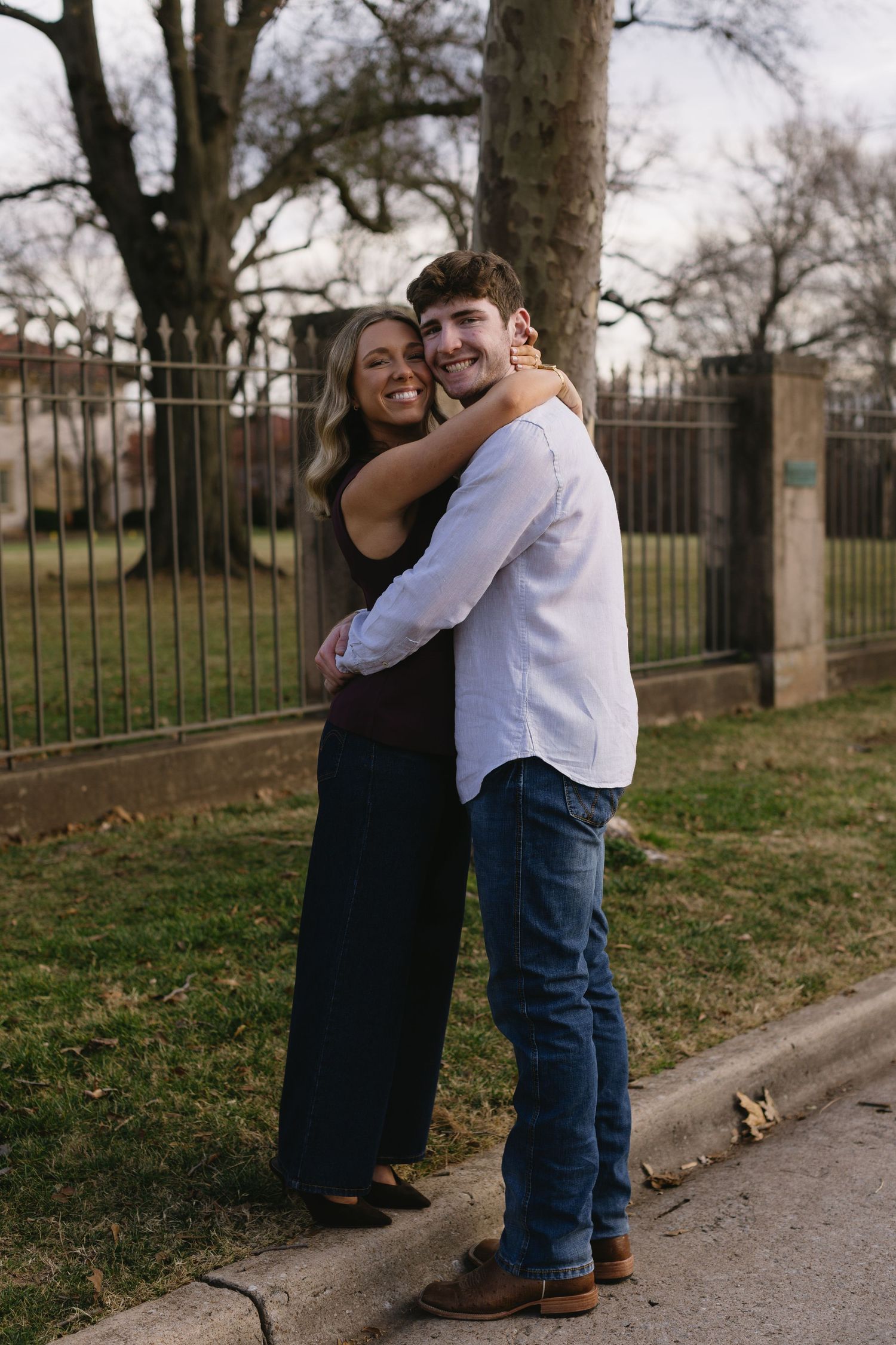 Couple embracing and laughing together on a path near a wrought iron fence.