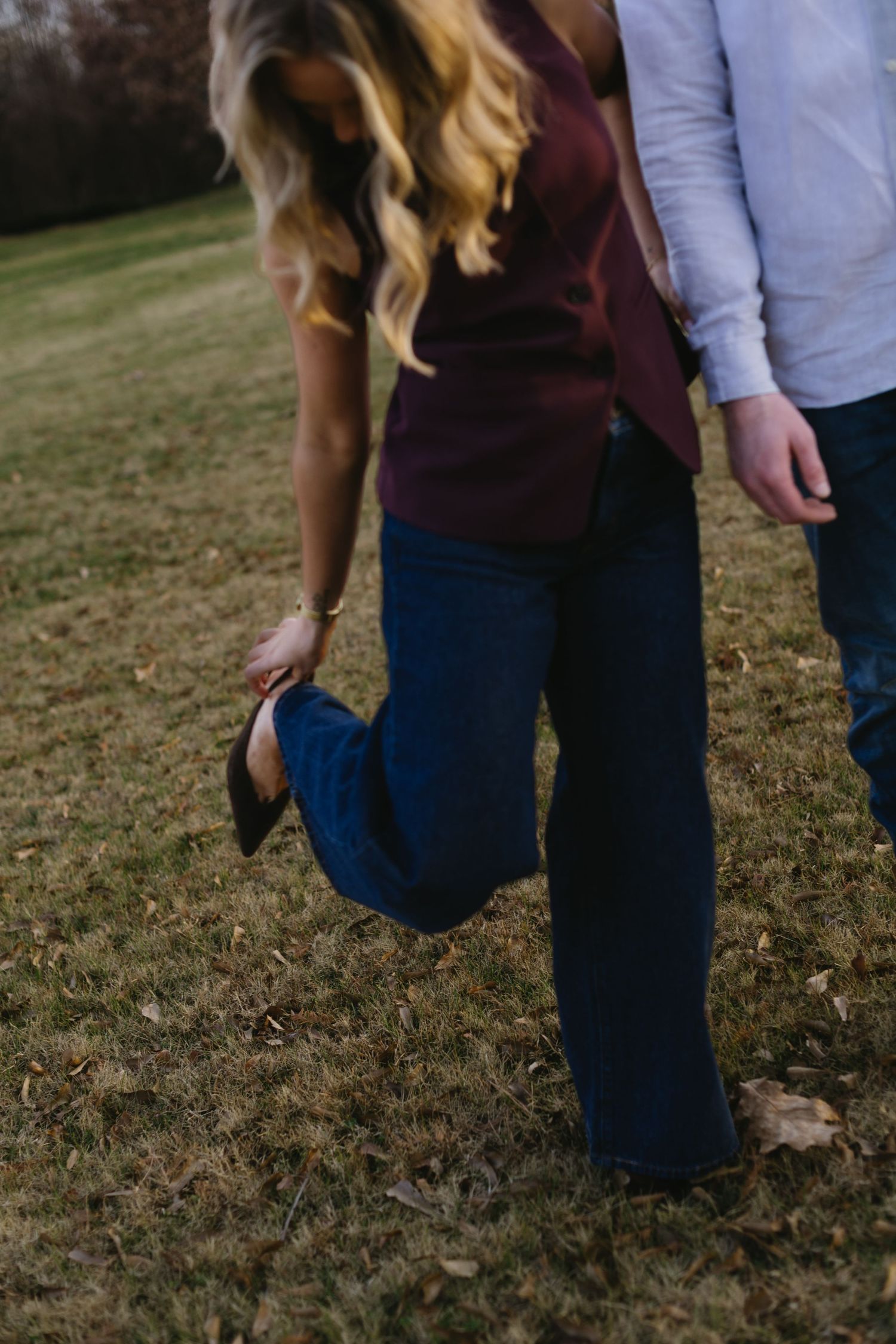 A casual couple photographed from waist down showing jeans and shoes while standing on grass.