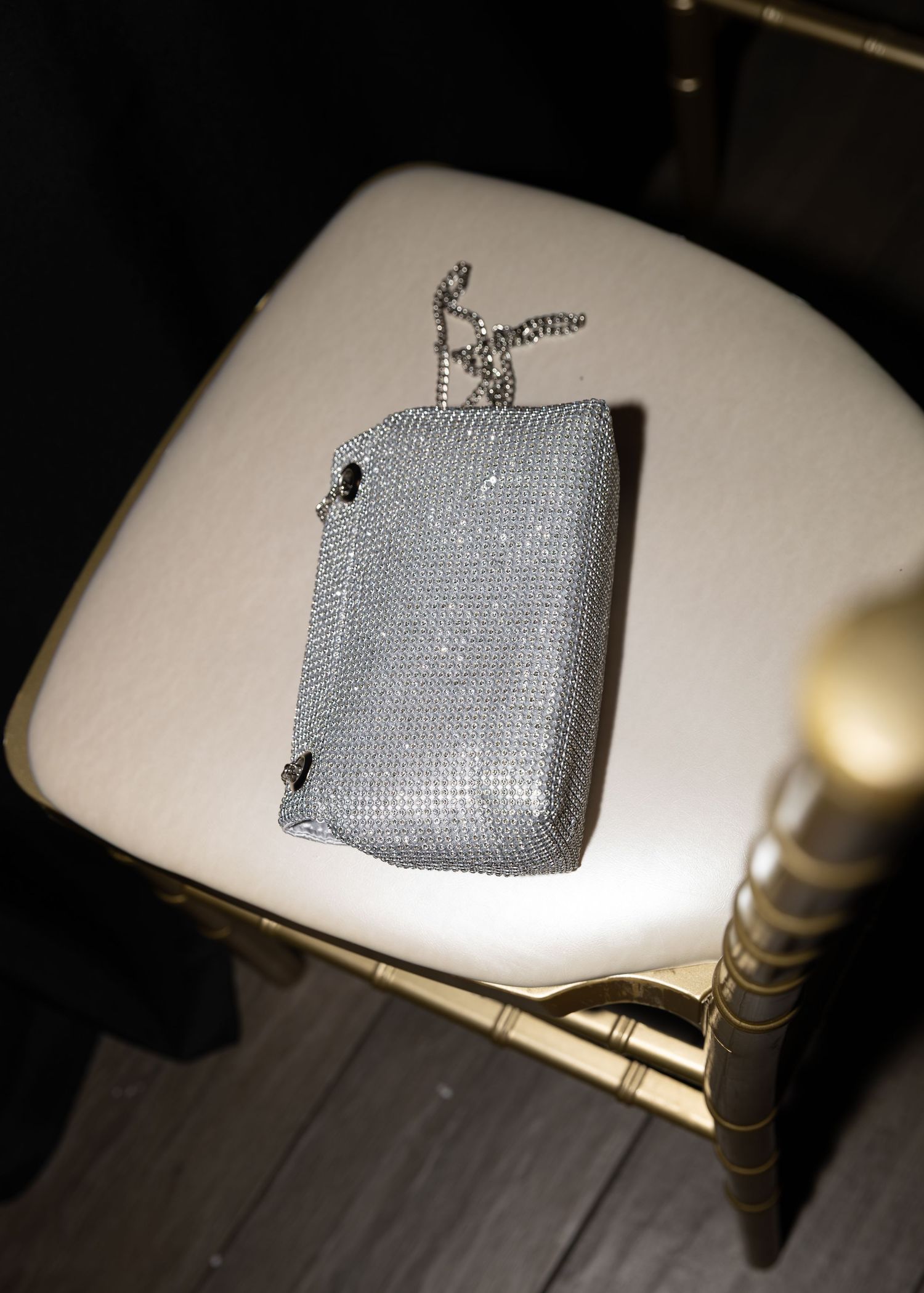 A sparkly silver evening clutch purse sits on a white chair at a formal event.