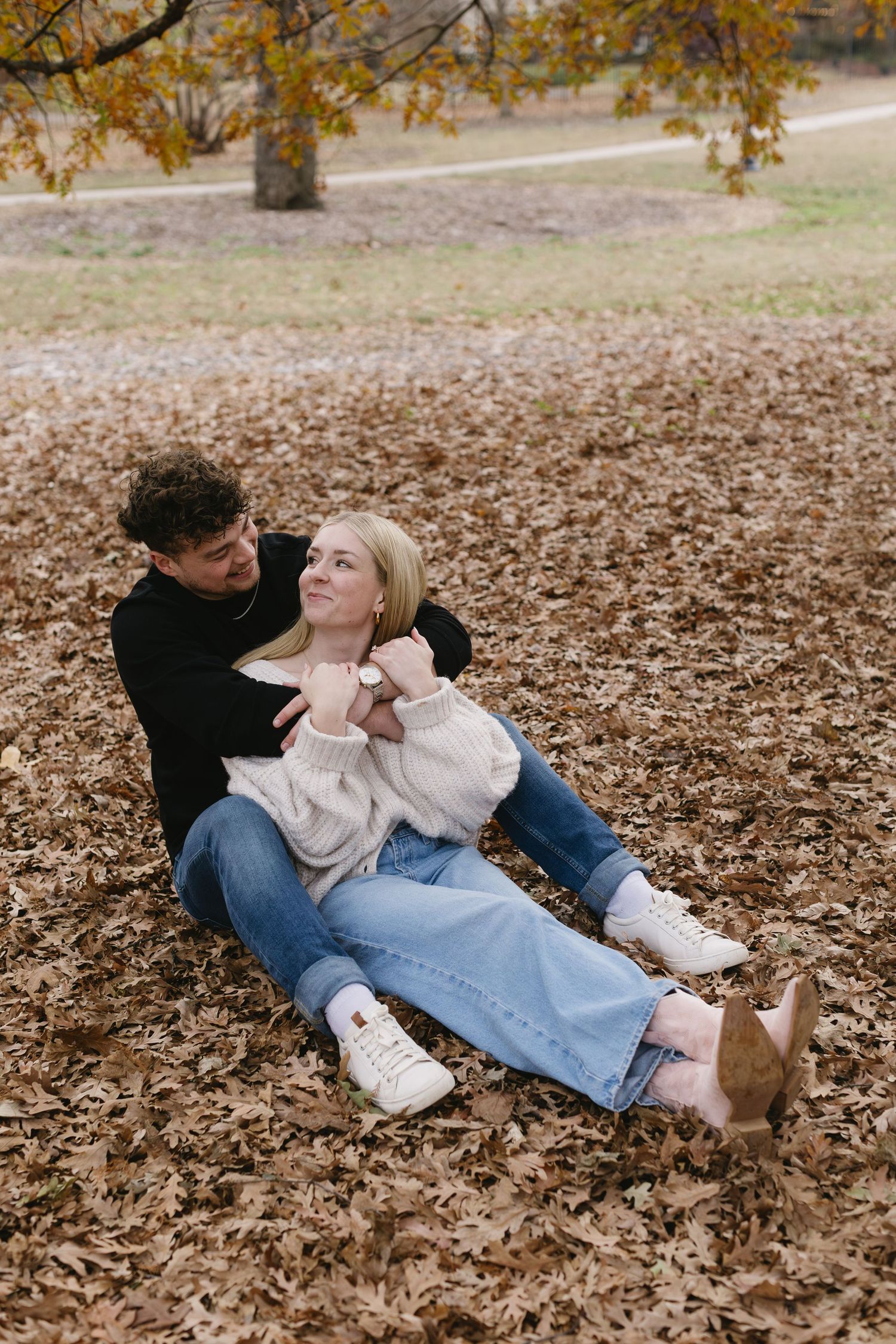 A couple relaxes together on a bed of fallen autumn leaves in a park setting.