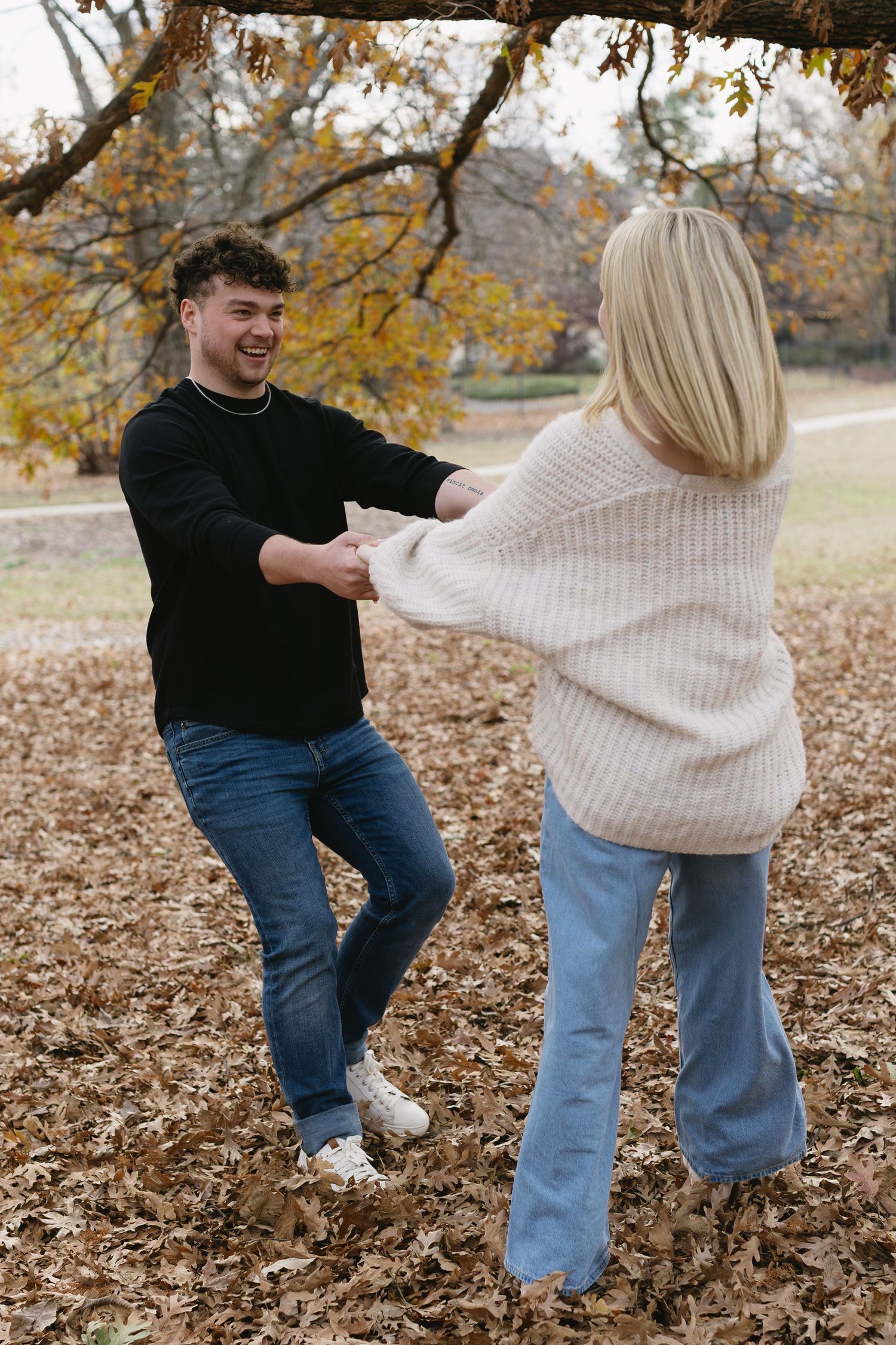 Playful autumn photoshoot with couple dancing in fallen leaves.